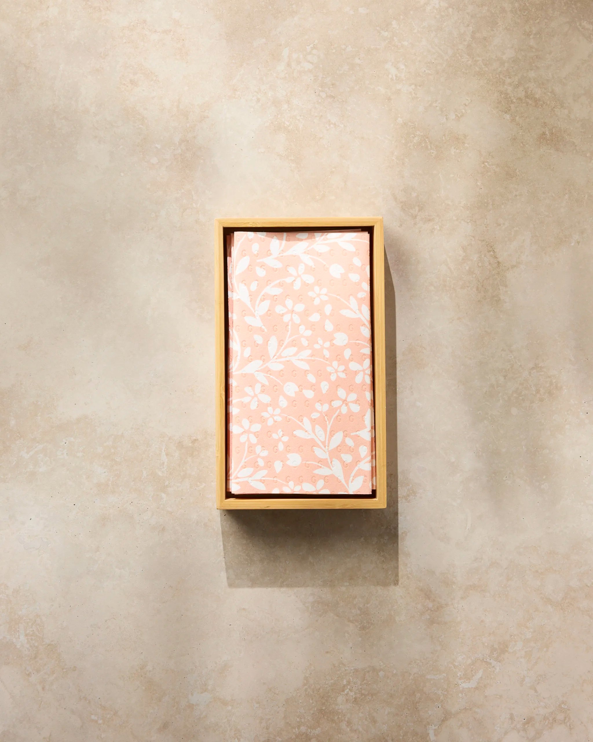 A rectangular box of Quiet Radiance paper towels by Geometry, featuring a peach lid with a white floral pattern, sits on a light beige marble surface.