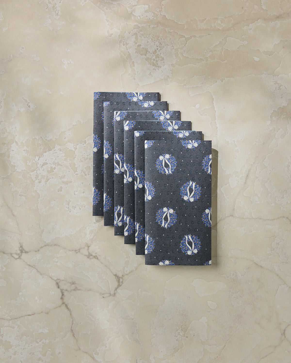 Eight playing cards with a blue and white circular pattern on a gray background are fanned out on a beige marble surface, their subtle texture reminiscent of the Quiet Skies eco-friendly kitchen towel by Geometry.