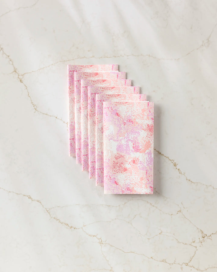 Seven rectangular Rawhide sheets by Elisabeth Wing, featuring a pink and purple abstract design, are neatly overlapped in a row on a lightly veined marble surface.