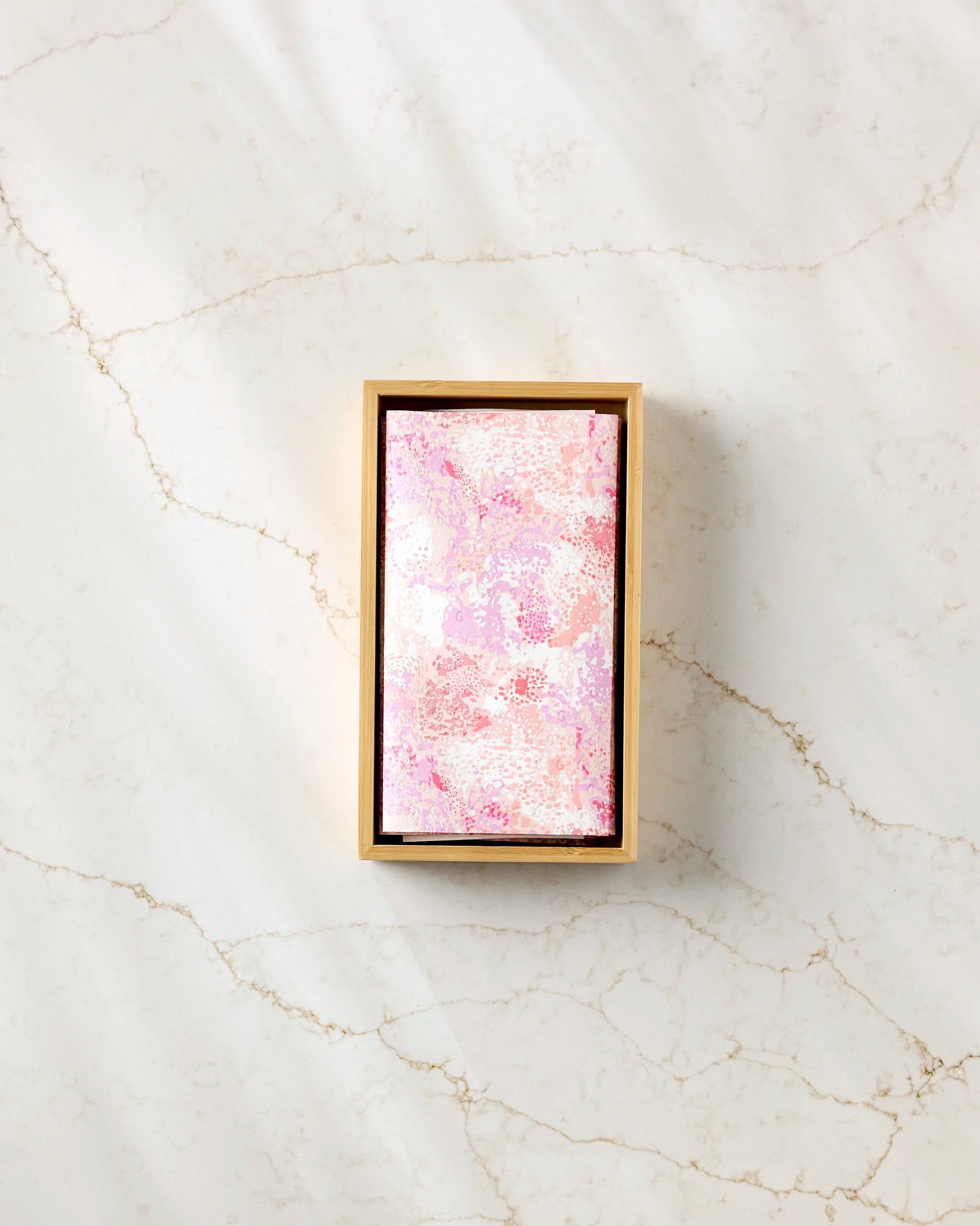 The Elisabeth Wing Rawhide is a rectangular box with a pink and white marbled lid, designed for storing eco-friendly kitchen towels or reusable paper towels, shown on a light marble surface.