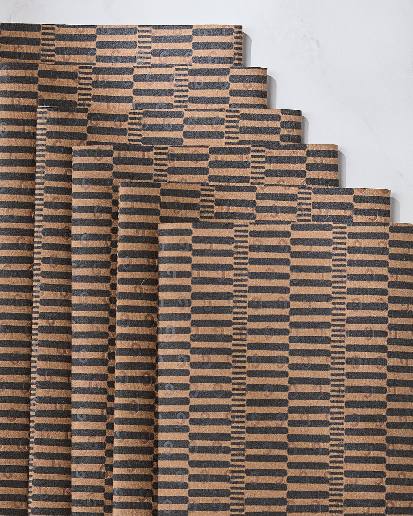 Five Geometry Ridge rectangular brown cutting boards with black geometric stripe patterns are fanned out on white marble, adding an eco-friendly kitchen vibe—perfect to pair with your favorite reusable paper towels.
