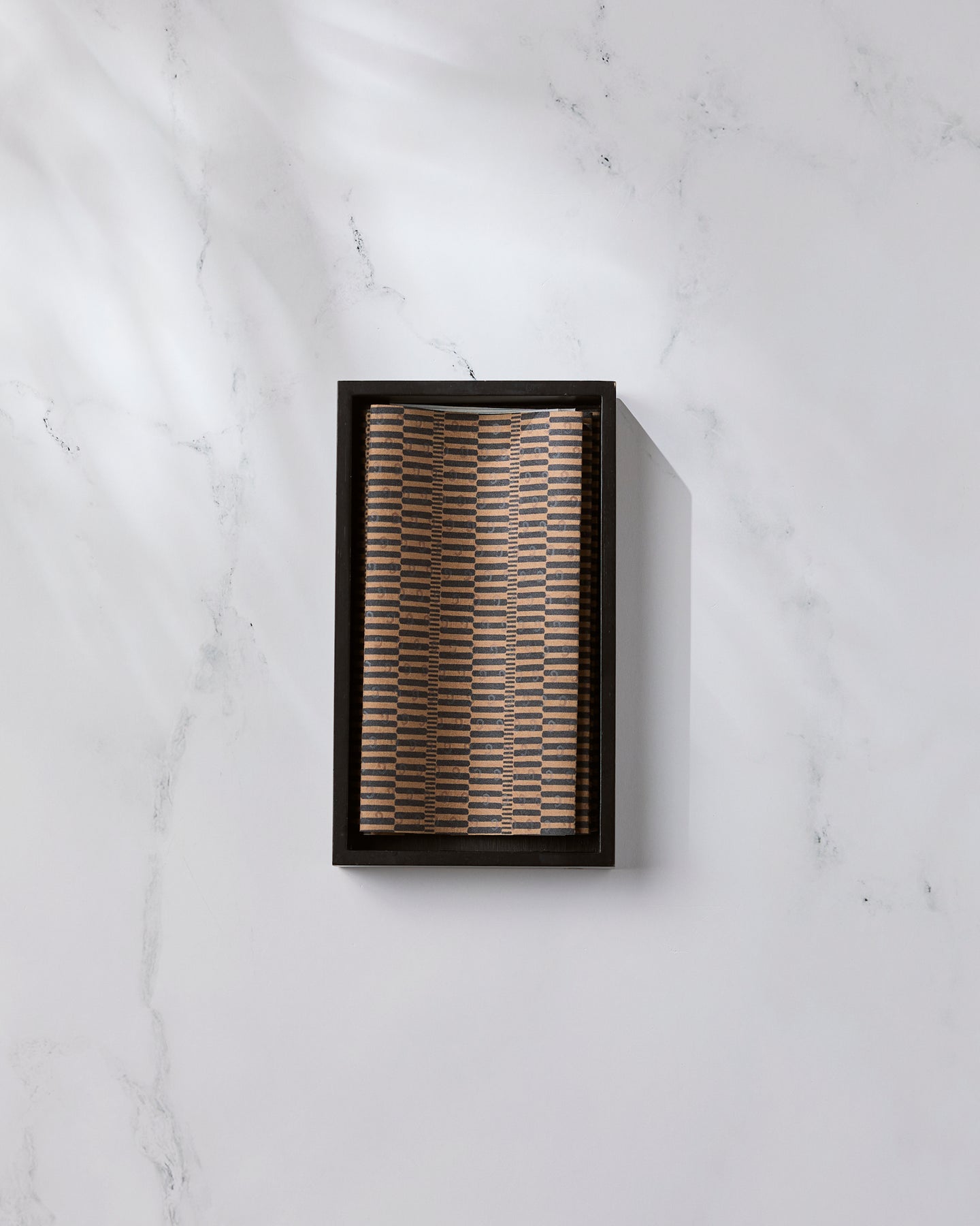 A rectangular box of Ridge eco-friendly kitchen towels by Geometry, featuring a woven patterned lid, rests on white marble with light reflections and subtle veining casting a soft shadow to the right.