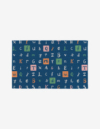 The School Days rug by Amy MacCready is a blue rectangular mat with colorful scattered uppercase and lowercase letters, some highlighted in orange, green, and pink boxes, made from post-consumer recycled materials for eco-friendliness.