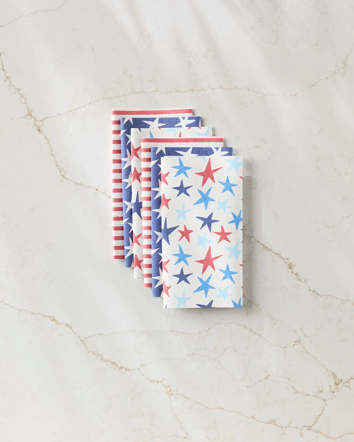 Four folded Mindfulnice Seeing Stars reusable paper towels are stacked on a light marble surface, featuring red, white, and blue star and stripe patterns for a patriotic Americana look. These eco-friendly napkins are perfect for your kitchen.