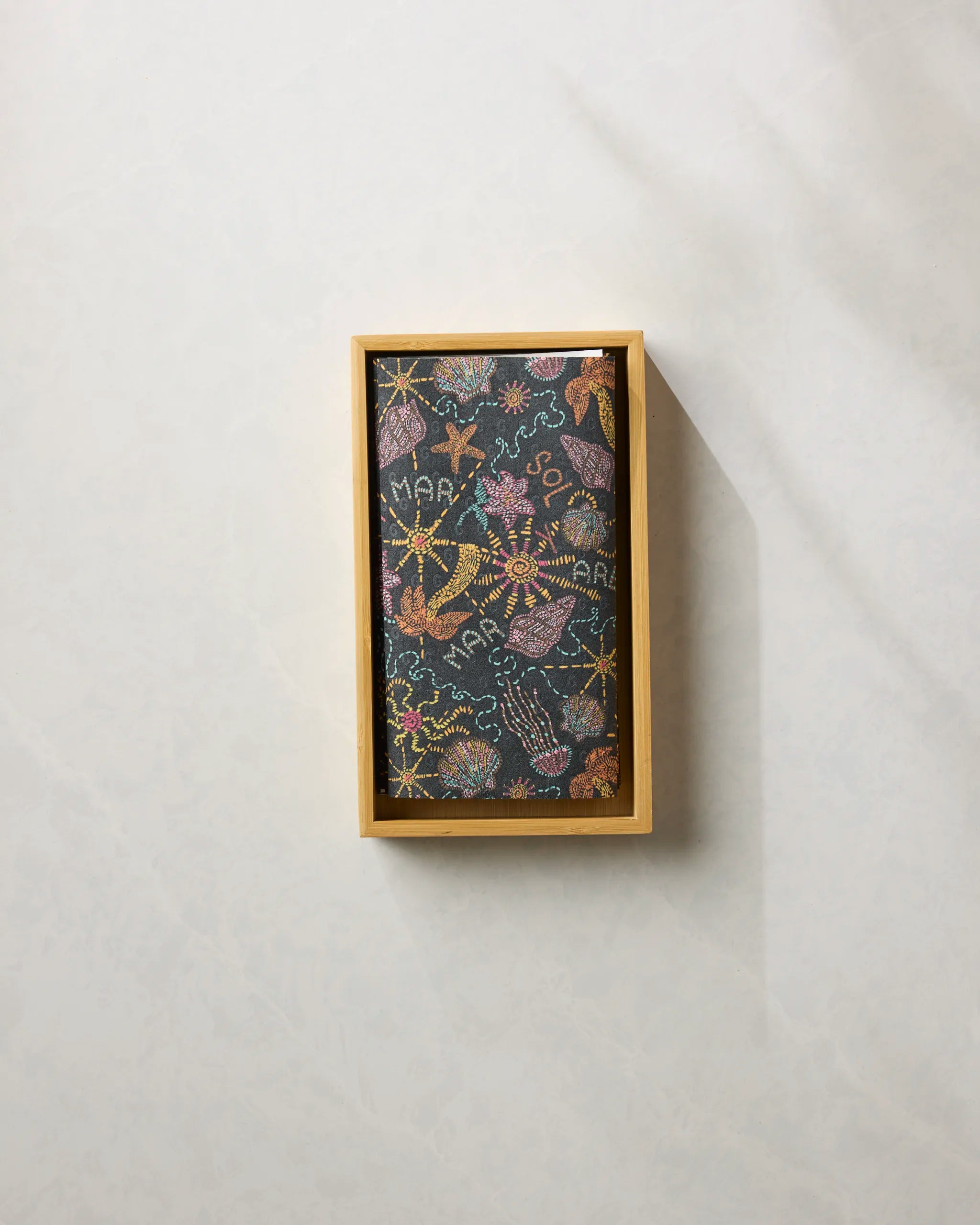 The Sol Mar Black by Geometry is a rectangular black scarf with embroidered sea creatures and MARA text, neatly folded in a wooden box—an ideal sustainable accent when paired with eco-friendly kitchen towels.