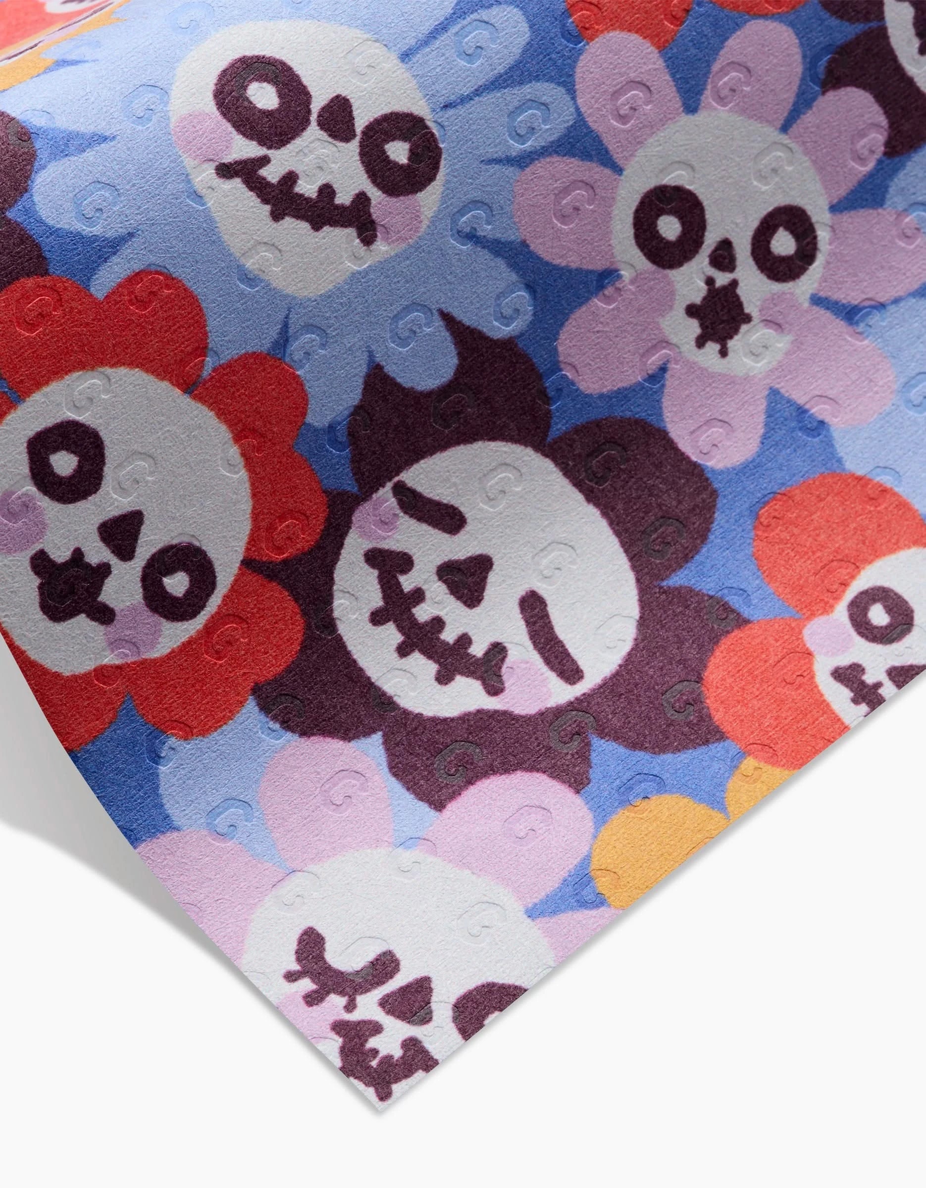 So Lazo’s Spooky Bouquet is a recycled paper towel with cartoon skull faces and floral petals in red, purple, and pink on a blue background, inspired by Day of the Dead motifs.