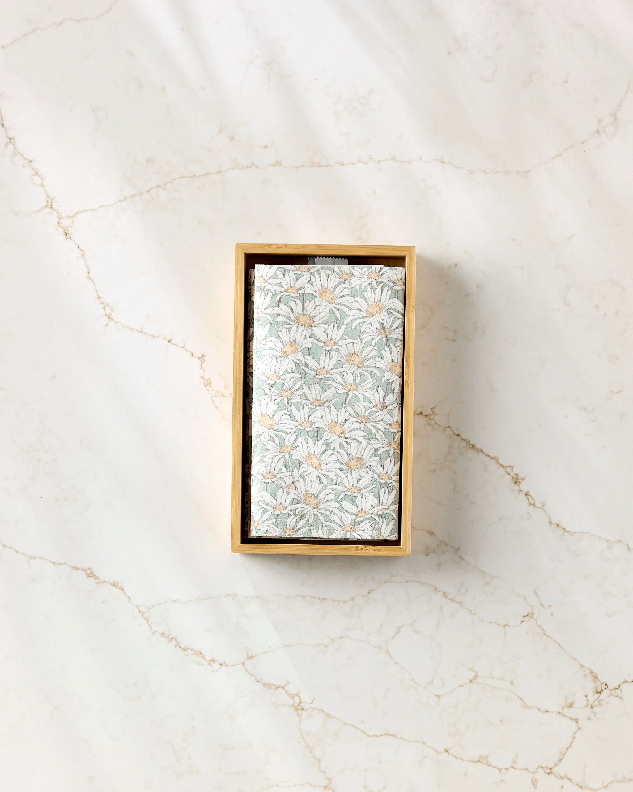 The "Springtime" rectangular box by Aubrey Fairchild features a floral-patterned lid with white and beige flowers and green leaves, making it a stylish way to store eco-friendly paper towels on any marble surface.