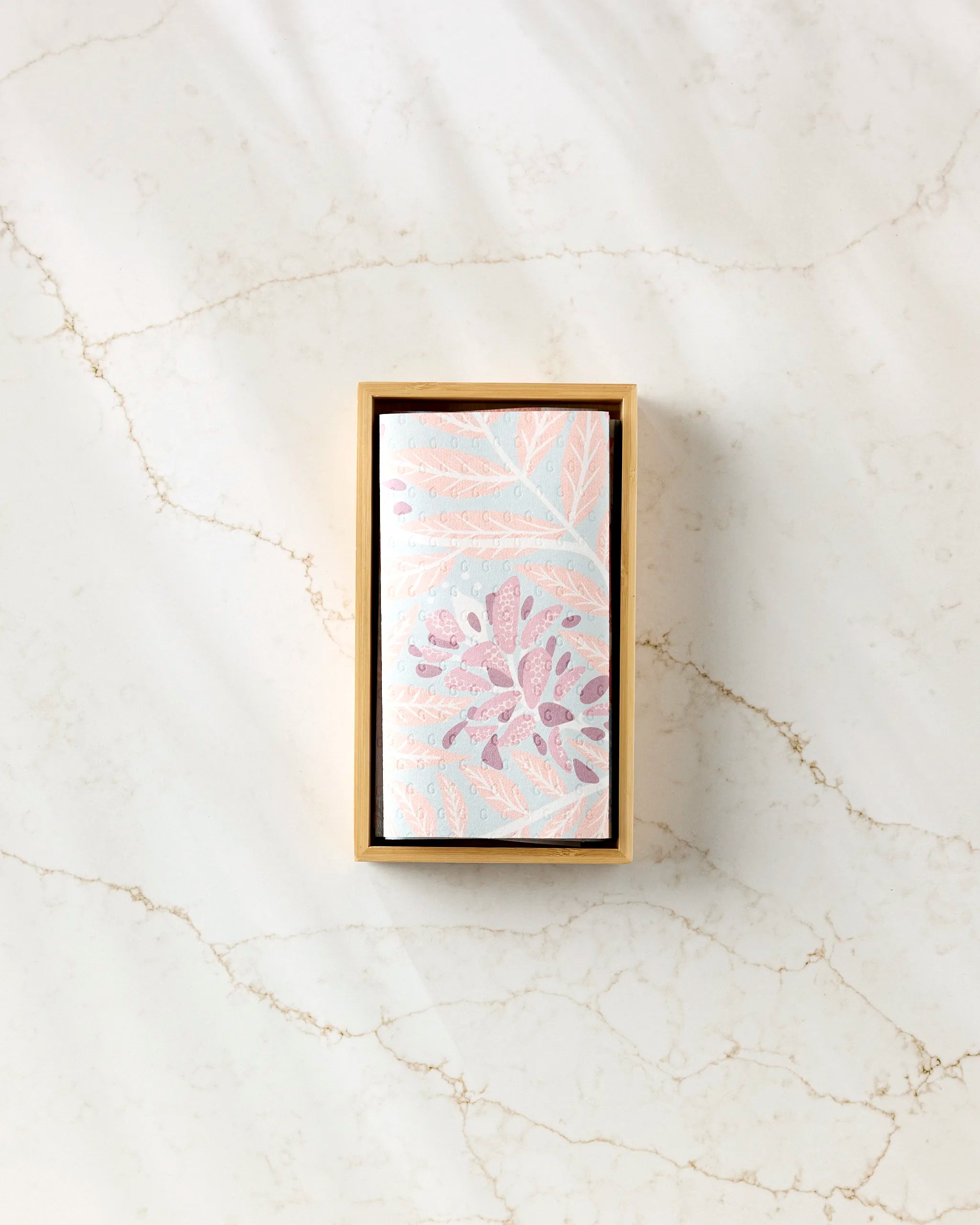 A rectangular State Flowers box by Julianne Haness, holding a floral-patterned reusable paper towel in pastel pink, blue, and purple leaves, displayed on a white marble surface with light brown veining.