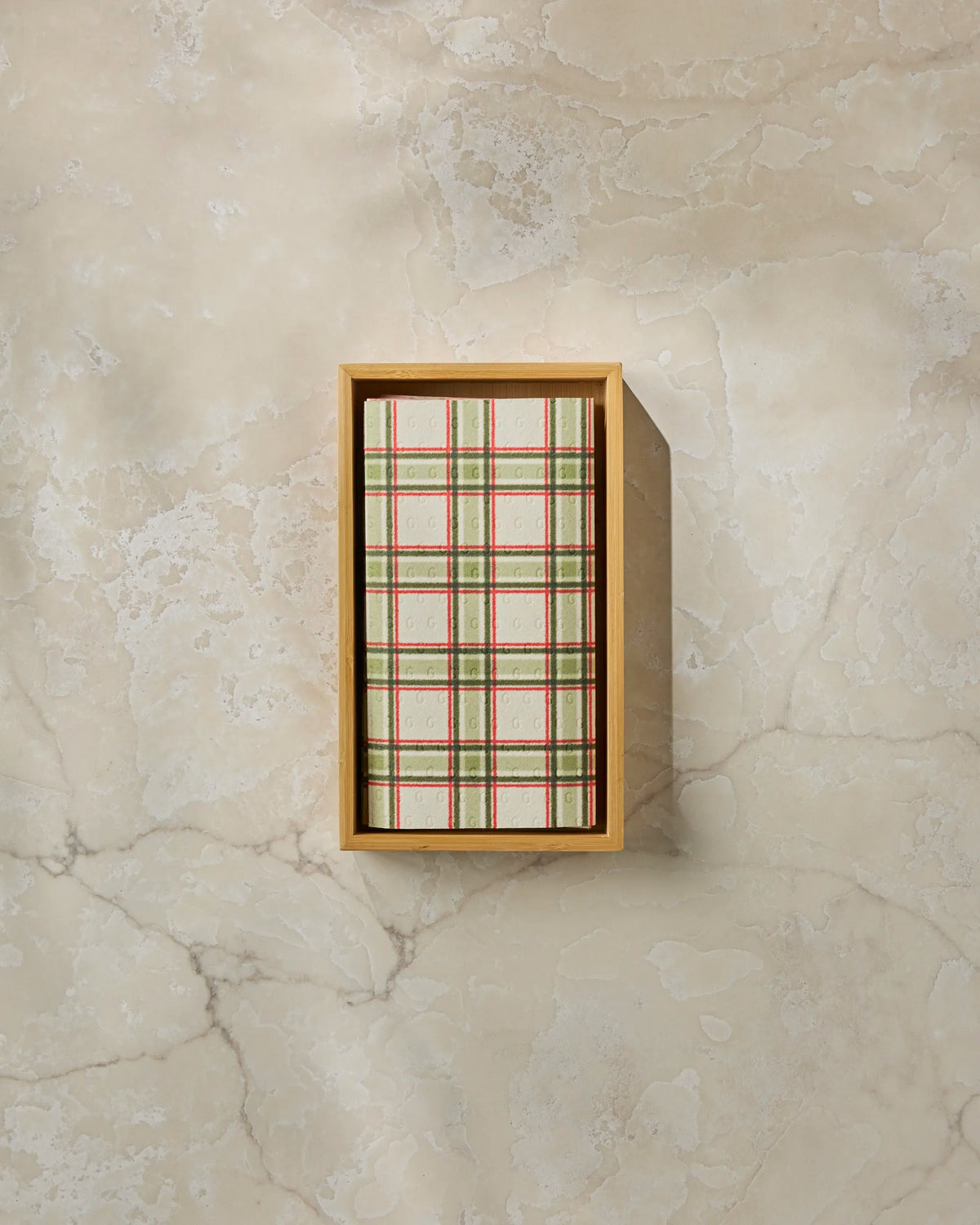 A rectangular box of Geometry’s Stocking Plaid kitchen towels rests on a beige marble surface, viewed from above.