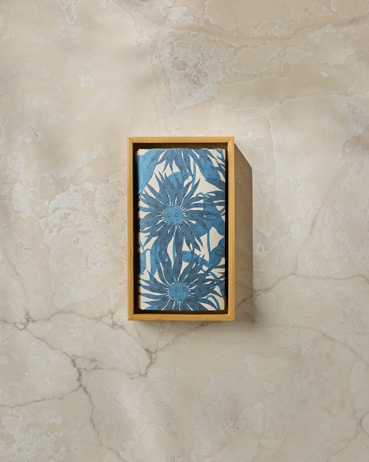 A rectangular bar of blue Sundara Frost soap featuring a delicate floral pattern rests in a wooden tray on a light beige marble surface, accompanied by Geometry’s eco-friendly kitchen towels—a perfect recycled paper towel alternative for a sustainable home.