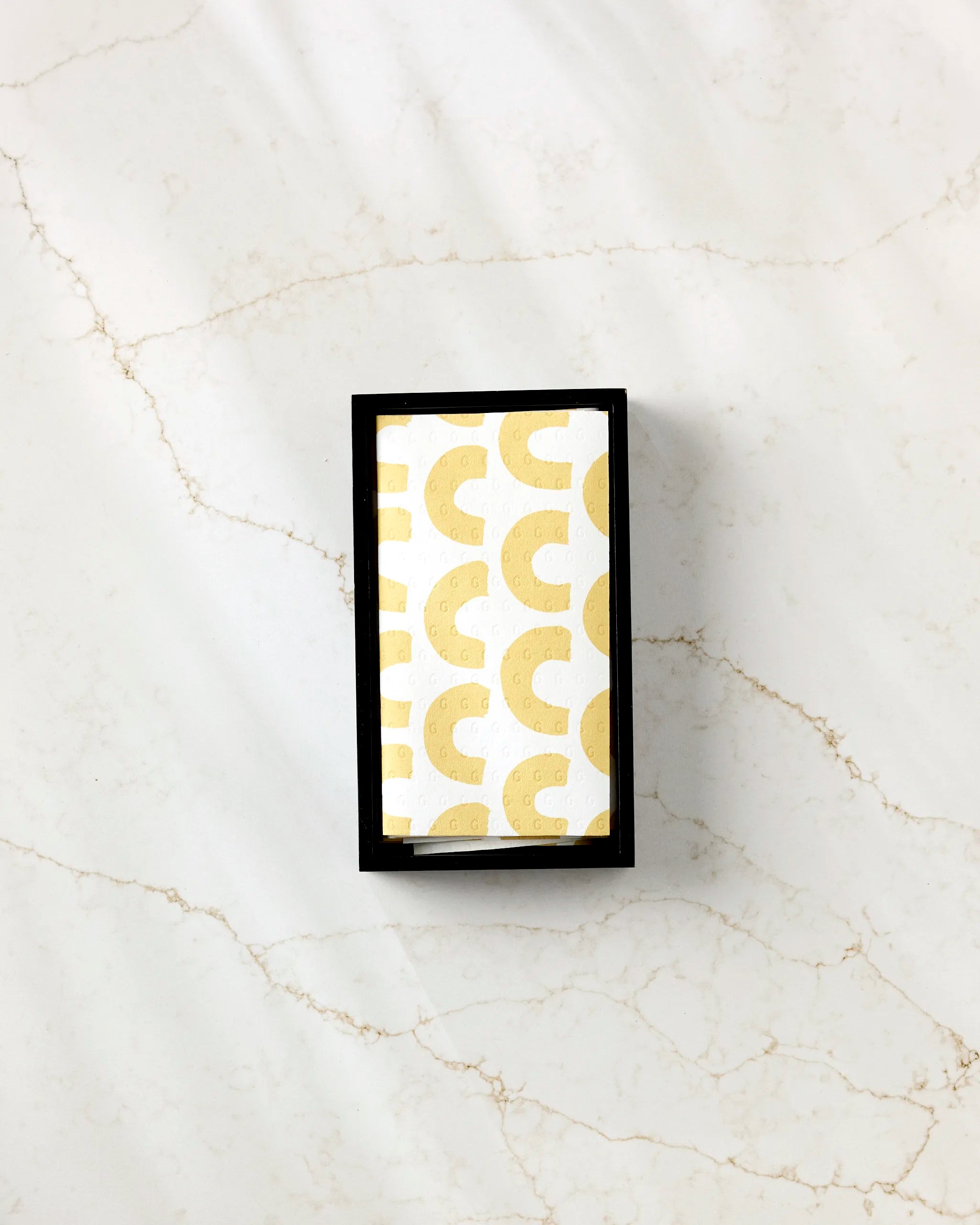 The GEOMETRY Sunny Hills box is a small rectangle with a white card inside and a repeating gold abstract pattern. Placed on veined white marble, it’s ideal for storing eco-friendly paper towels.