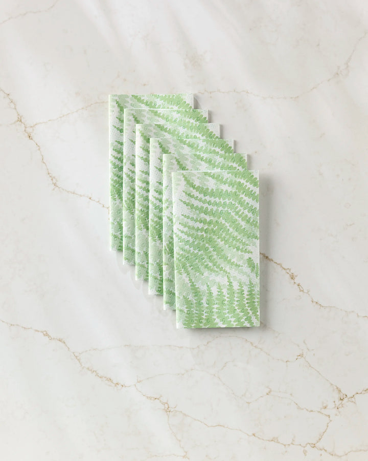 Six Swaying Leaf napkins by GEOMETRY, featuring a green leaf pattern inspired by eco-friendly kitchen towels, are arranged neatly on a white marble surface with beige veining.