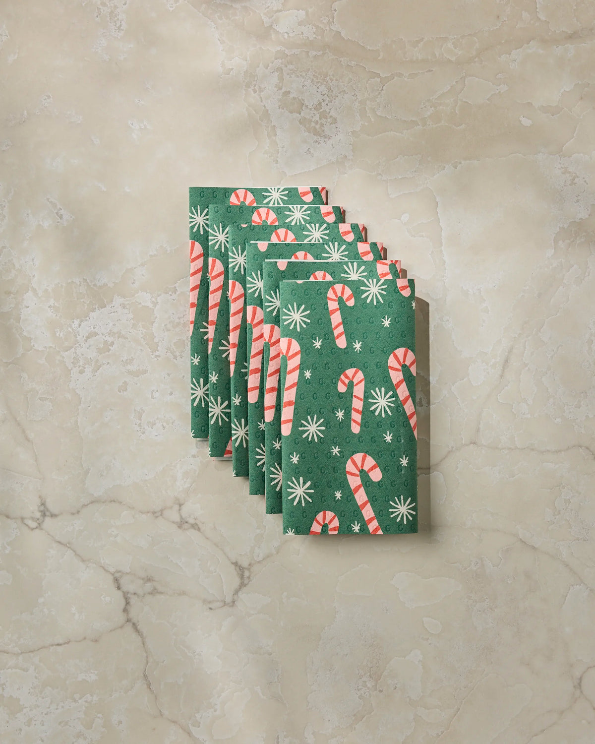 Seven “Sweet Candy” cards by Geometry, featuring red and white candy canes and white snowflakes on a green background, are fanned out on a beige marble surface—capturing the cheerful spirit of the season and pairing perfectly with your eco-friendly kitchen towels.