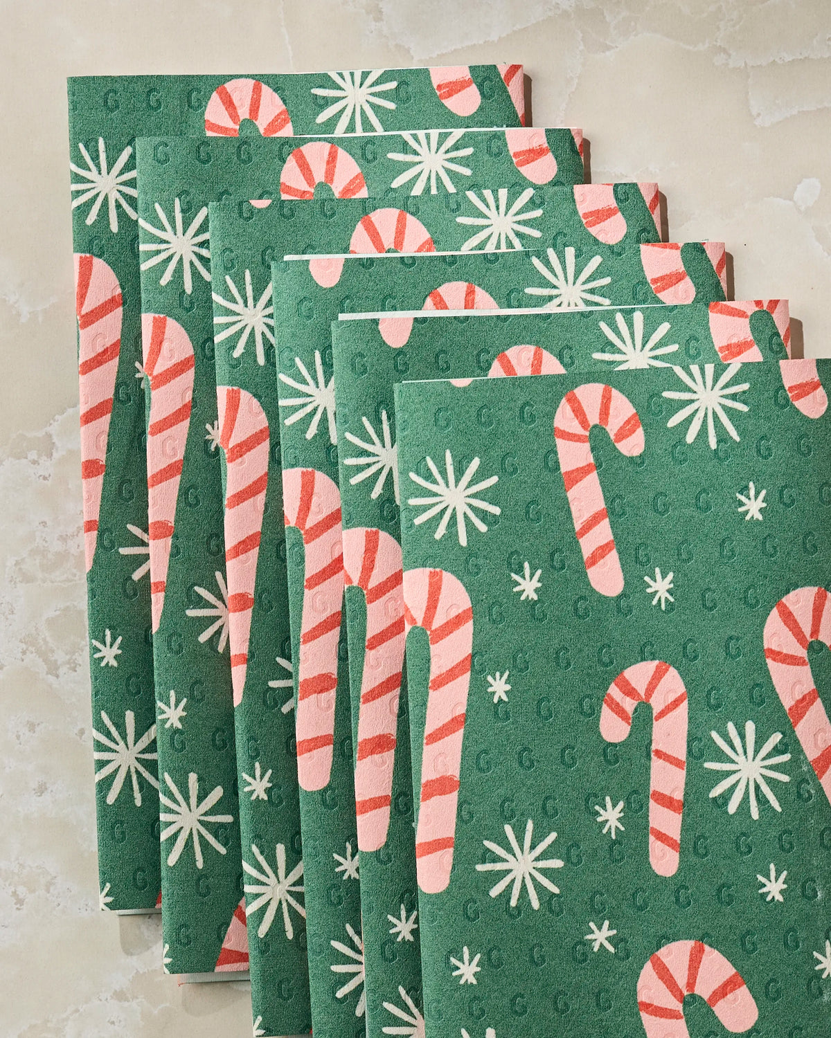 Six “Sweet Candy” napkins by Geometry, featuring green fabric with red and white candy canes and white snowflakes, are stacked on a light-colored surface—delivering a festive, eco-friendly kitchen towel option that serves as the perfect alternative to recycled paper towels.