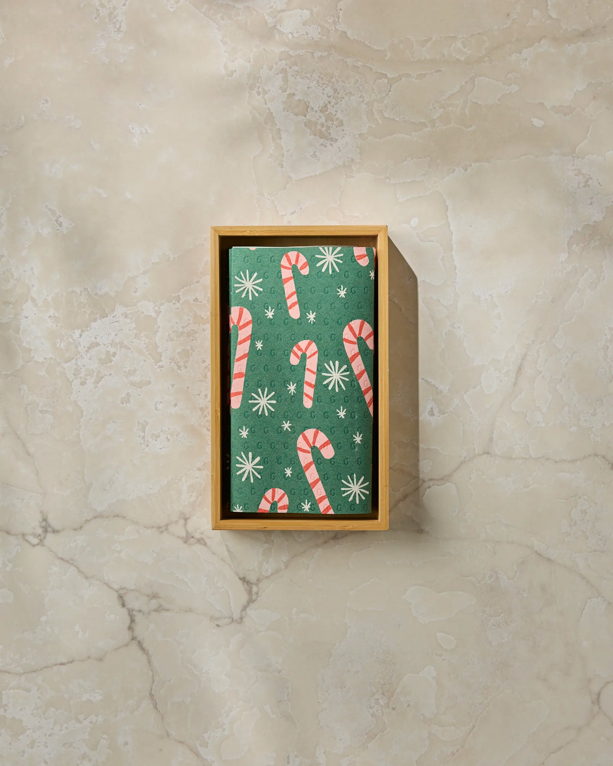 A rectangular wooden box holds Geometry Sweet Candy green reusable paper towels decorated with red and white candy canes and white snowflakes, placed on a beige marble surface.