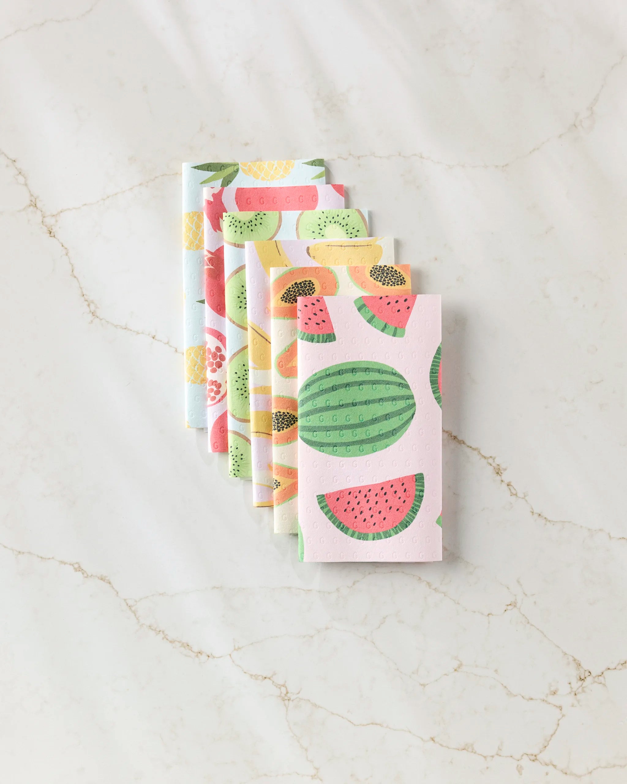 Six GEOMETRY Sweet Summer Mix 2 reusable rectangular paper towels with colorful fruit patterns—watermelon, kiwi, lemon, and strawberries—are stacked overlapping on a white marble surface.