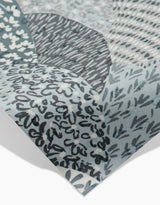 Close-up of a Sweet Valley Hills Green sheet by Hufton Studio, featuring abstract gray, blue, and white patterns with hand-drawn lines, dots, and leaf shapes. The corner is slightly lifted—ideal as an eco-friendly kitchen towel.