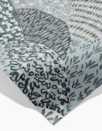 Close-up of a Sweet Valley Hills Green sheet by Hufton Studio, featuring abstract gray, blue, and white patterns with hand-drawn lines, dots, and leaf shapes. The corner is slightly lifted—ideal as an eco-friendly kitchen towel.