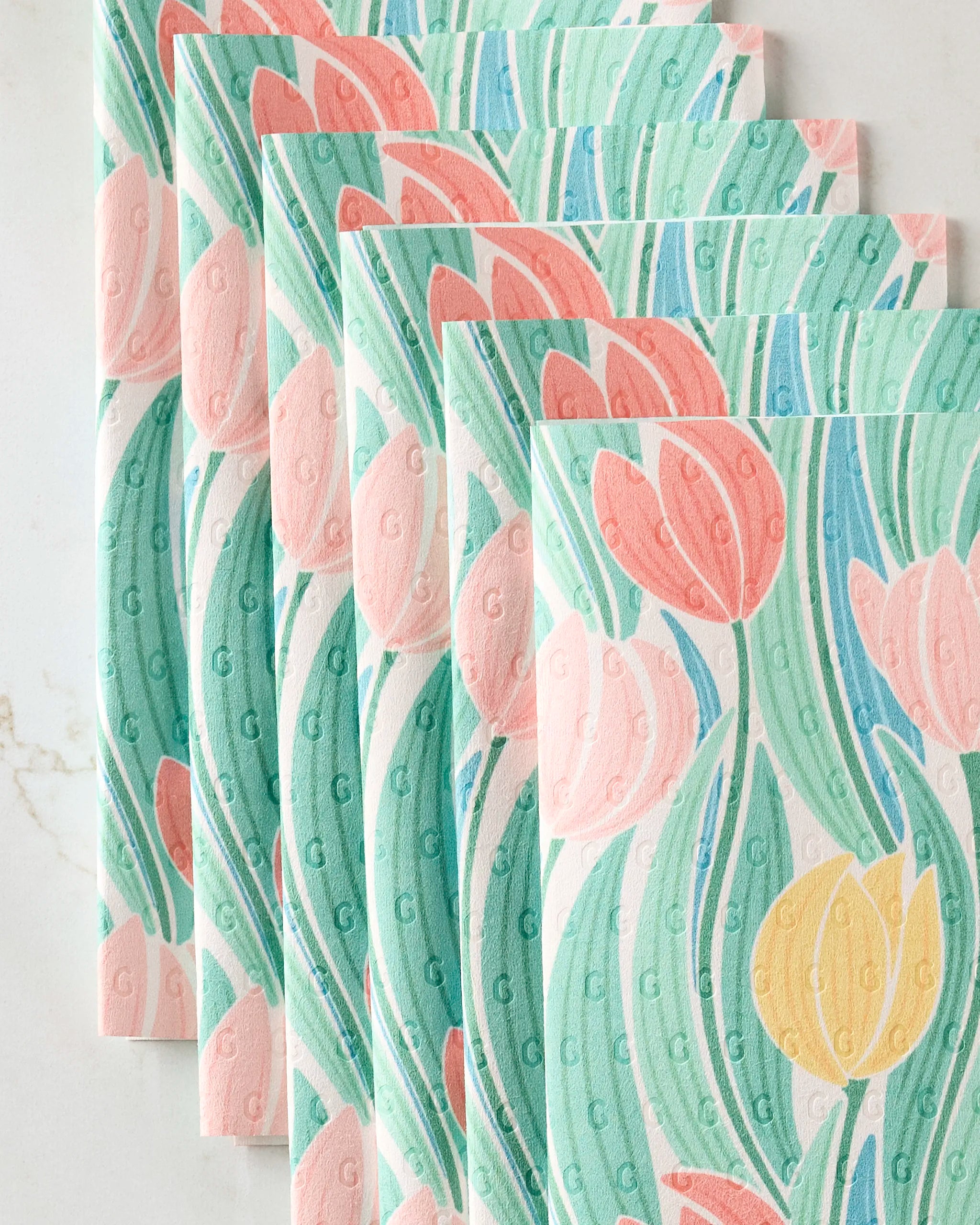 Five Tranquil Tulips eco-friendly paper napkins by Sarah Daugherty, featuring a colorful floral design with pink, coral, yellow, and blue tulips and green leaves, are neatly stacked on a light surface.