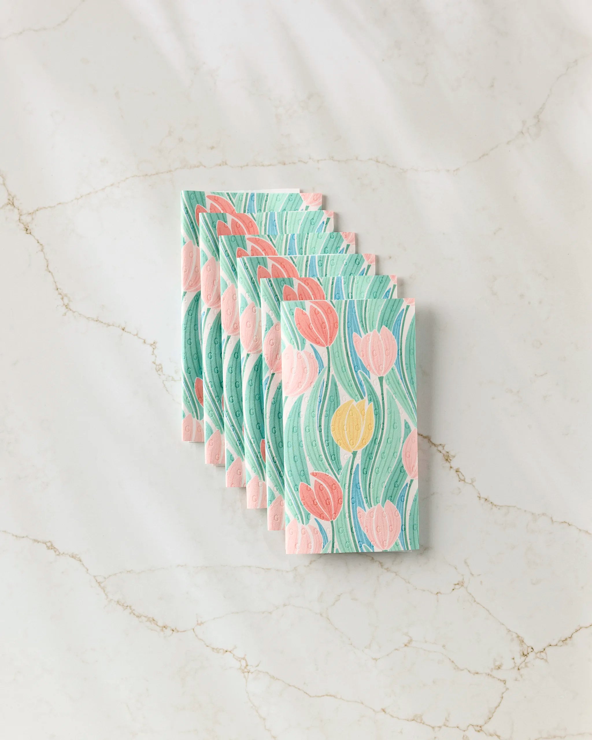 Six Tranquil Tulips rectangular reusable paper towels by Sarah Daugherty, featuring a pastel tulip pattern in pink, yellow, and green, are stacked neatly and offset on a marble surface.