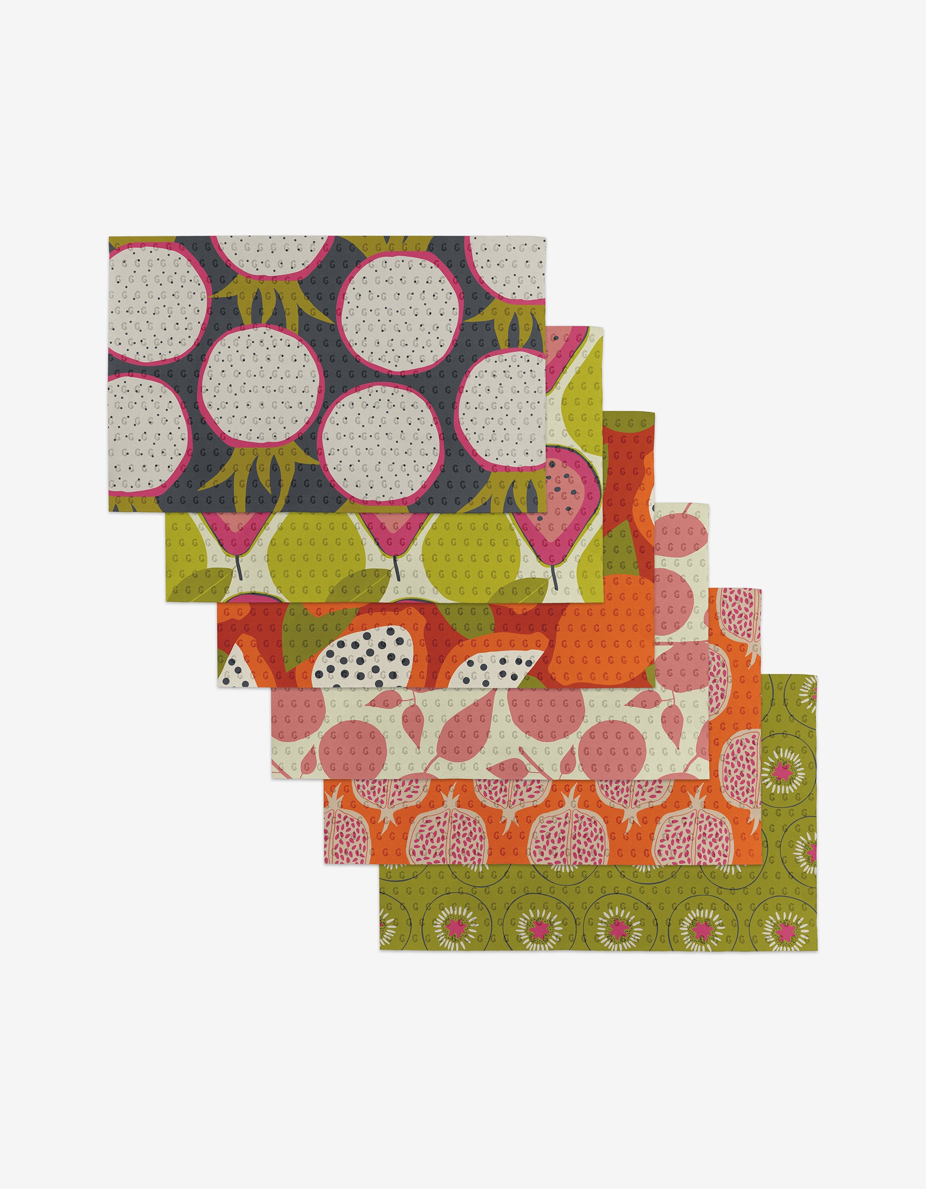 Six Lizzie Clark Tropical Fruit placemats with vibrant green, orange, pink, and navy fruit patterns are fanned out on a white background—each made from eco-friendly materials.