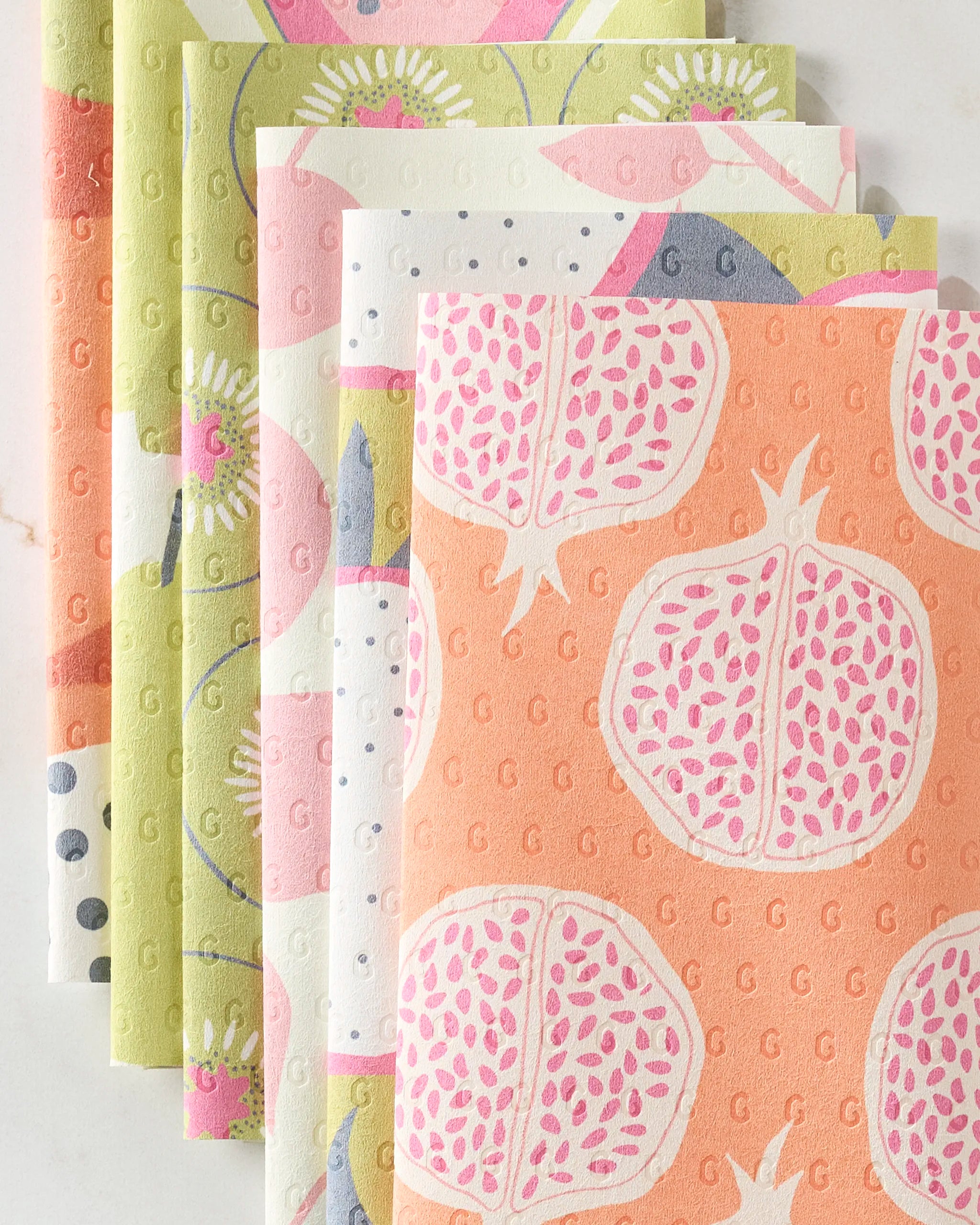 Five Lizzie Clark “Tropical Fruit” reusable paper towels with pomegranate and botanical patterns feature pastel green, orange, pink, white, and purple tones, arranged side by side.
