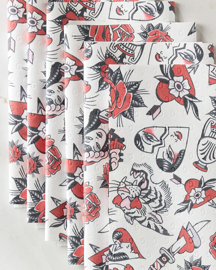 Valentine's Flash napkins by Cole Strem feature a tattoo-inspired print with roses, hearts, a tiger, and a woman's face in red, black, and gray on eco-friendly paper towels, fanned out for display.