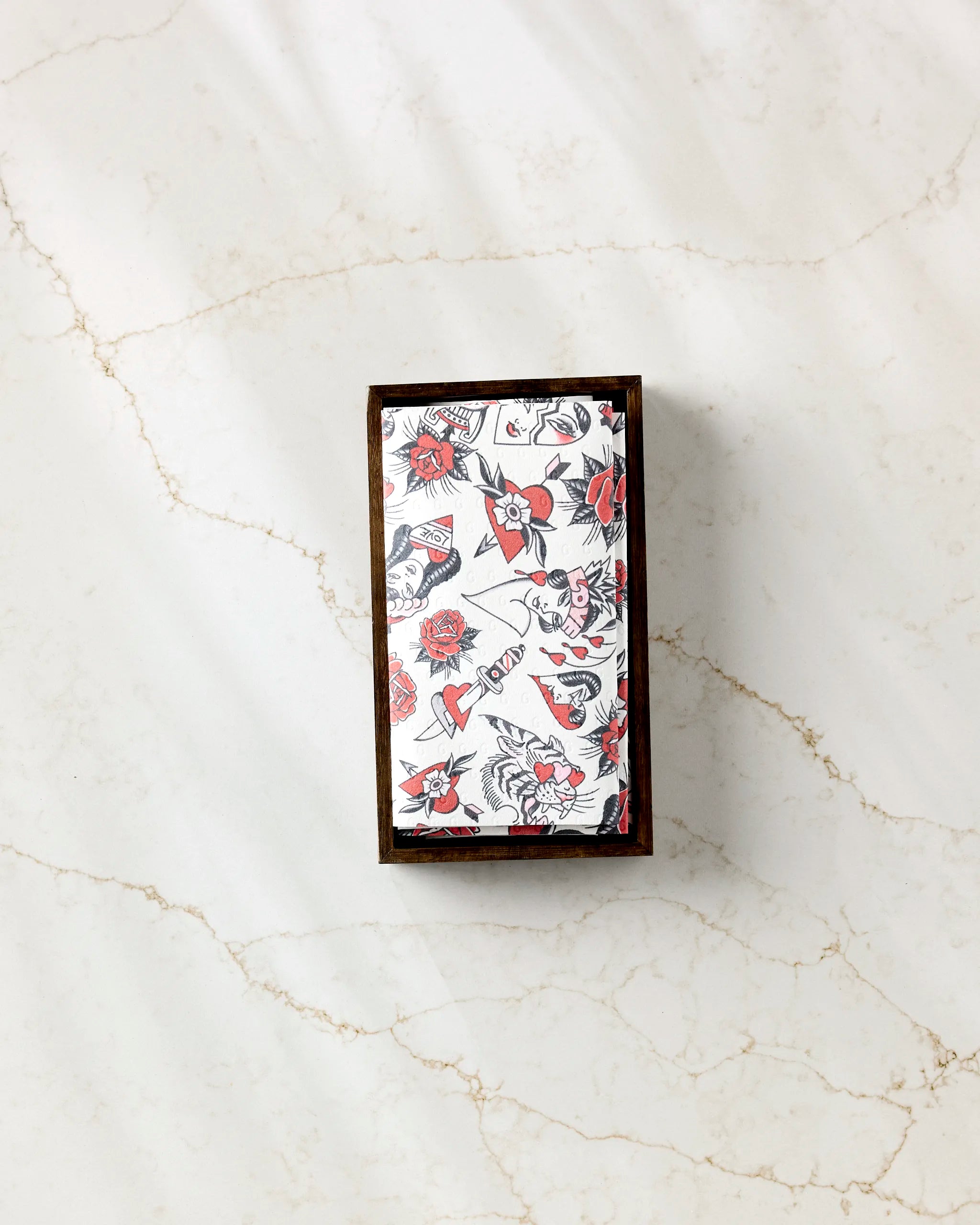 The Cole Strem "Valentine's Flash" box, featuring black and red tattoo-style roses, birds, and hearts, sits on a marble surface—perfect for stylishly storing your reusable paper towels.
