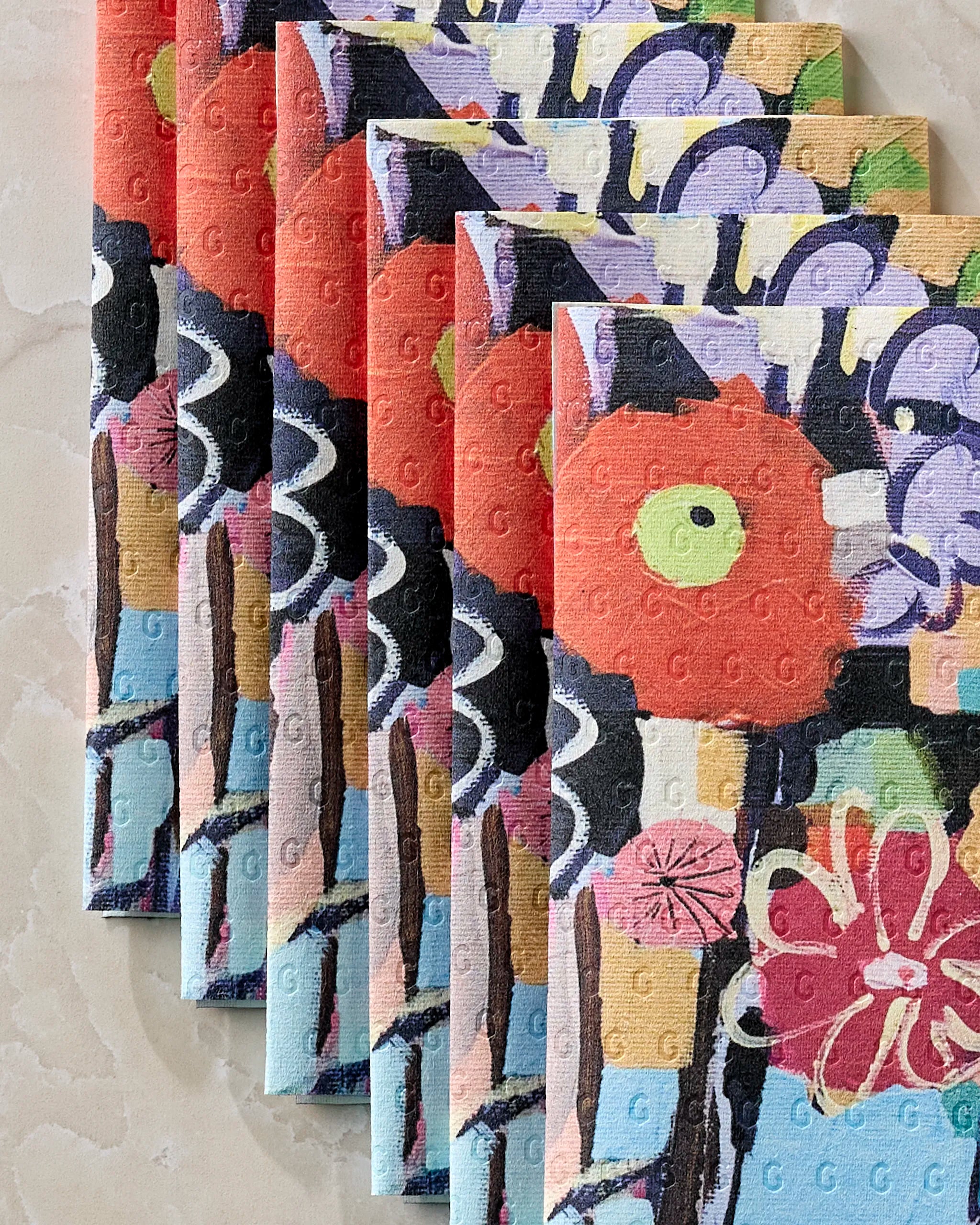 Five colorful Vera eco-friendly paper towels by Ania Zwara Art are fanned out on marble, each featuring abstract floral and geometric designs in red, purple, green, black, and white.