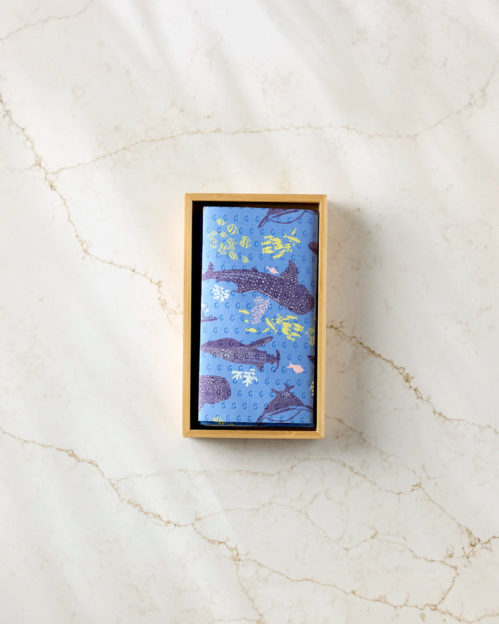 The Whale Shark reusable paper towels by Elisabeth Wing come in a rectangular box with a blue cloth featuring whale and sea plant illustrations—an eco-friendly alternative to disposables, elegantly shown on a light marble surface.