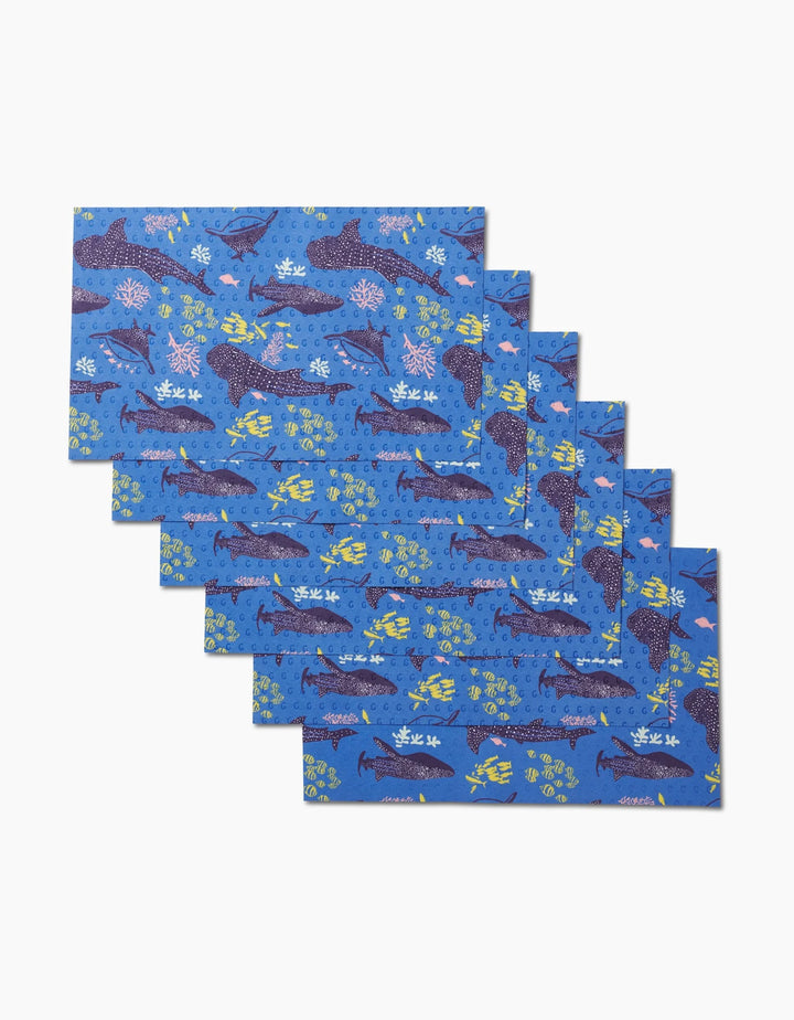 Six rectangular blue Whale Shark placemats by Elisabeth Wing feature vibrant sea creature designs—sharks, turtles, and coral—in a fanned-out stack. An eco-friendly, reusable alternative to Not Paper Towels.