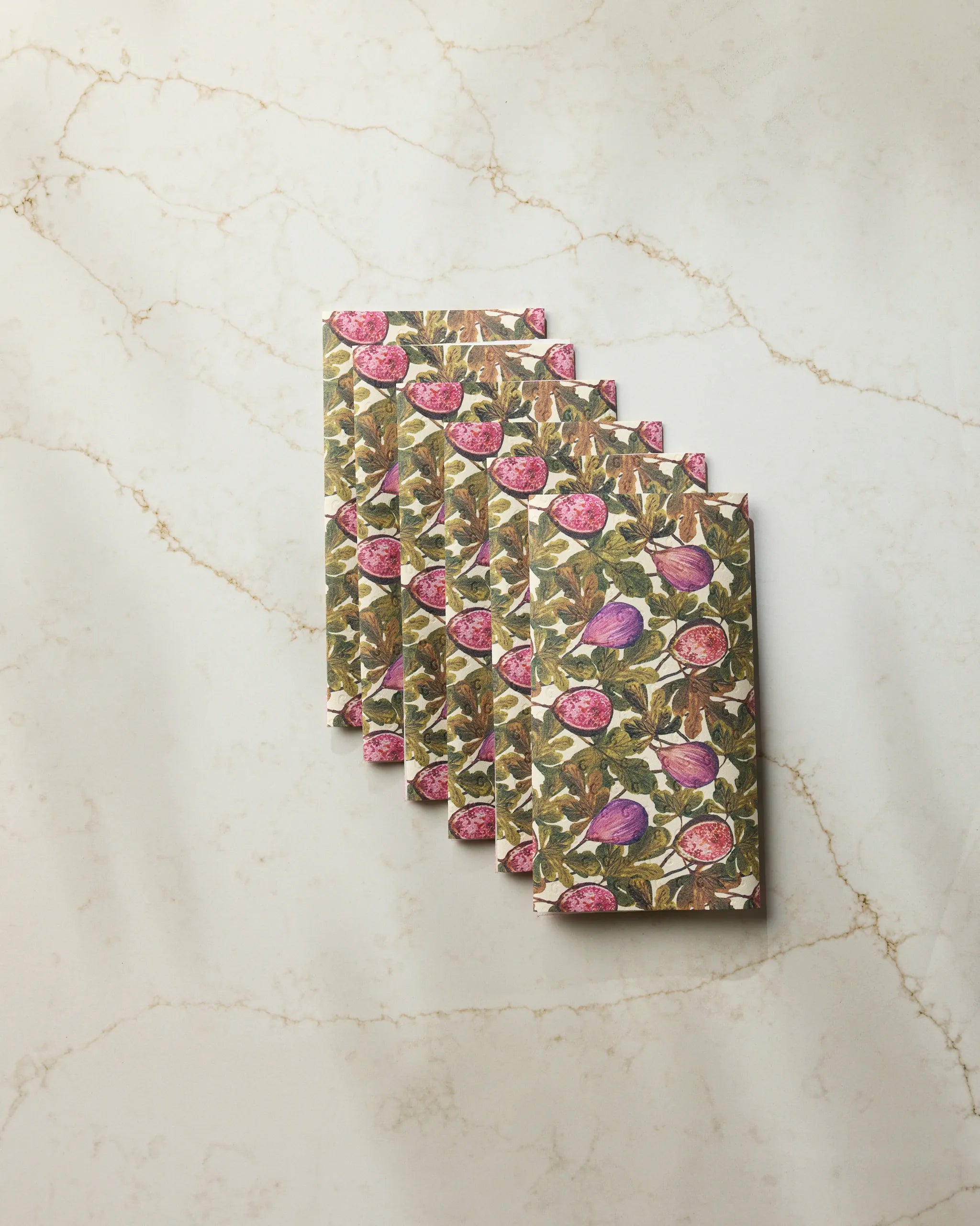 Five rectangular Geometry Wild Fig reusable paper towels, featuring a fig fruit pattern, are overlapped in a fan arrangement on a light marble surface.