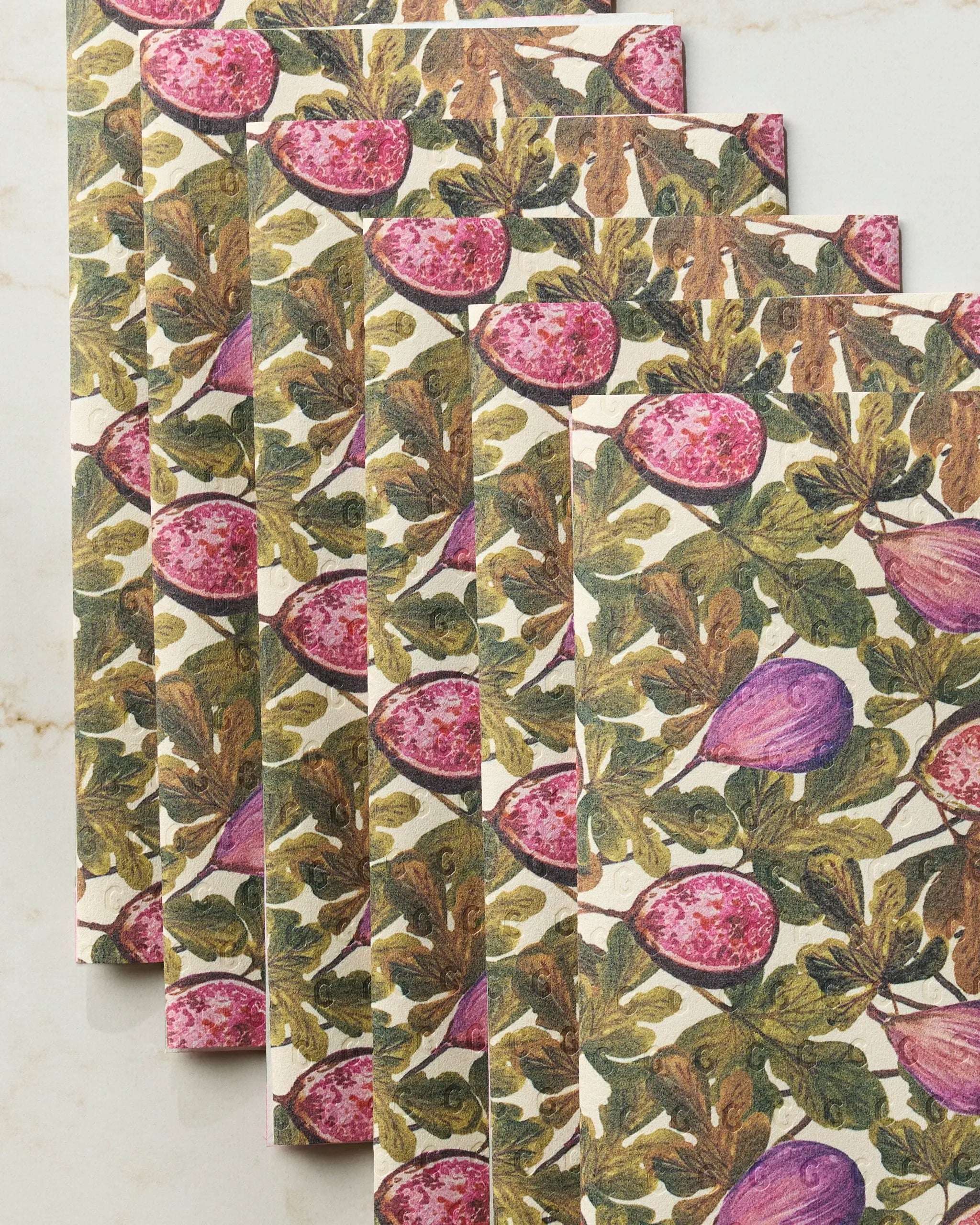 Five Geometry Wild Fig reusable rectangular paper towels, printed with purple figs and green leaves on white, are neatly fanned out on a light surface.