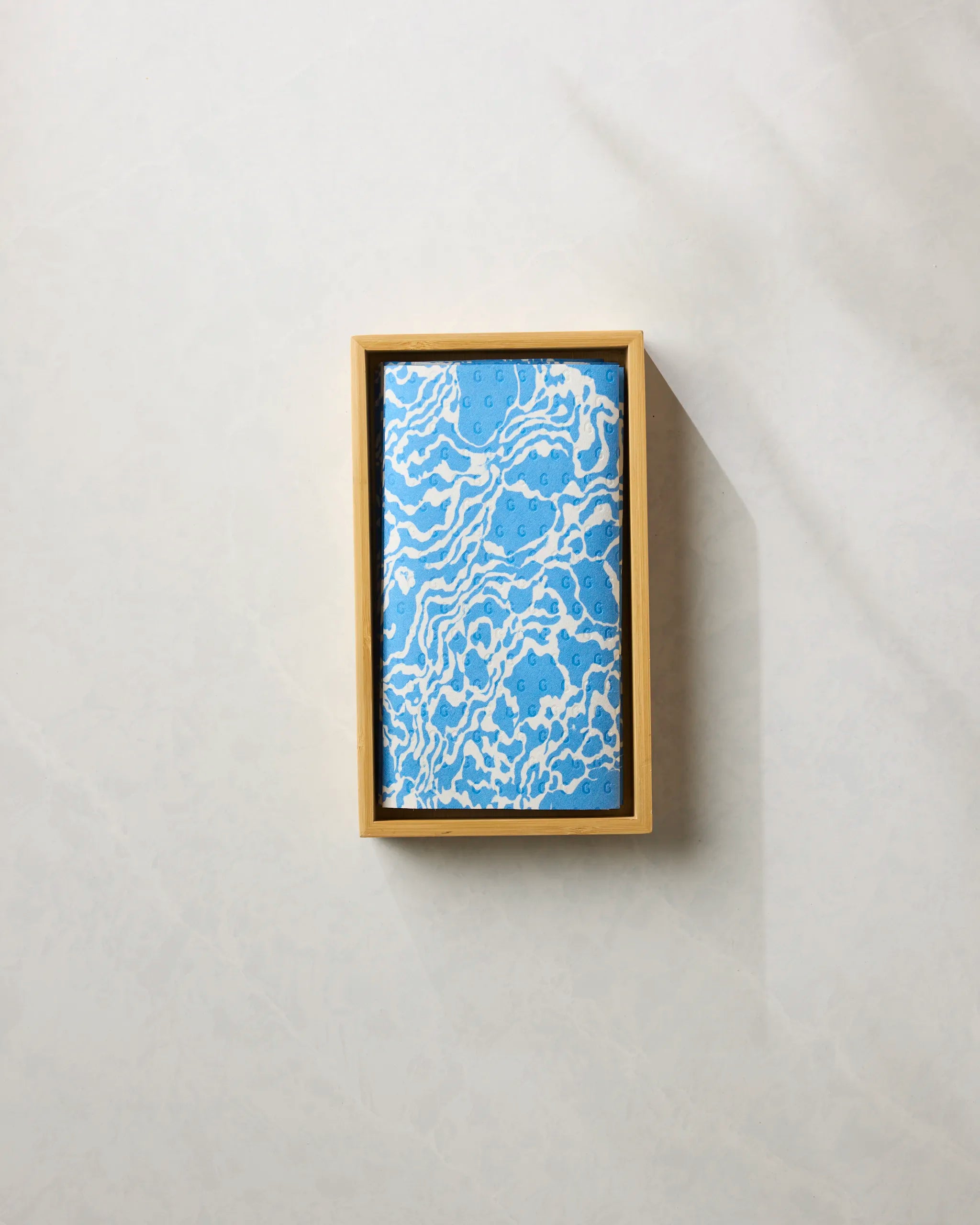 A rectangular wooden box displays the "Windward" reusable paper towels by Geometry, featuring a blue and white marbled pattern, set on a light textured surface.