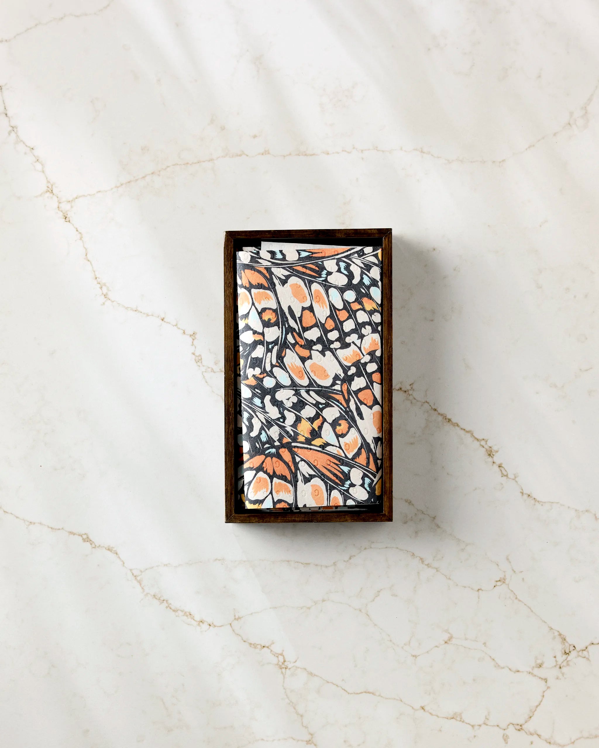 The GEOMETRY "Wings in the Wind" rectangular bar soap, featuring a detailed black, white, and orange butterfly wing design, sits on light marble near eco-friendly kitchen towels for a sustainable accent.