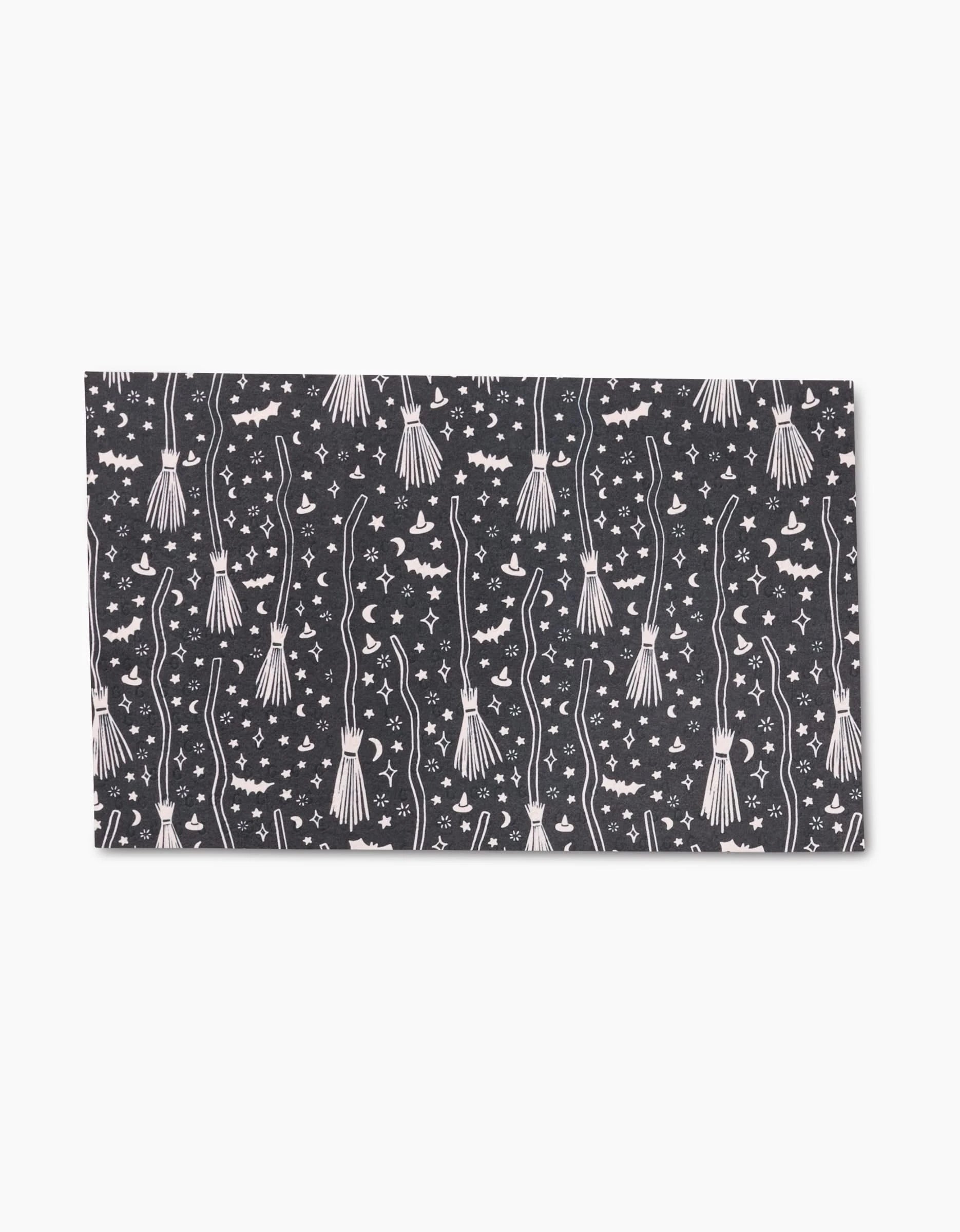 The Kayla Ann Witches Broom mat features a black background with white brooms, stars, and magical symbols—perfect for pairing with your eco-friendly kitchen towels for a touch of sustainable style.