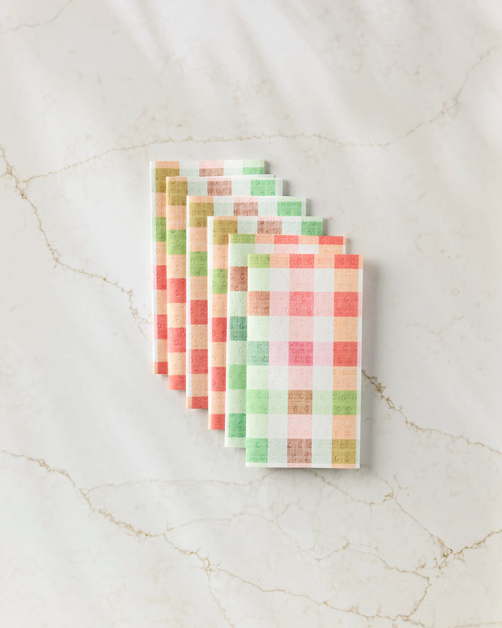 Six Pascale Dilger Woven Spring Plaid cloths in pastel pink, green, orange, and white are neatly fanned on a white marble surface—perfect as eco-friendly reusable paper towels.