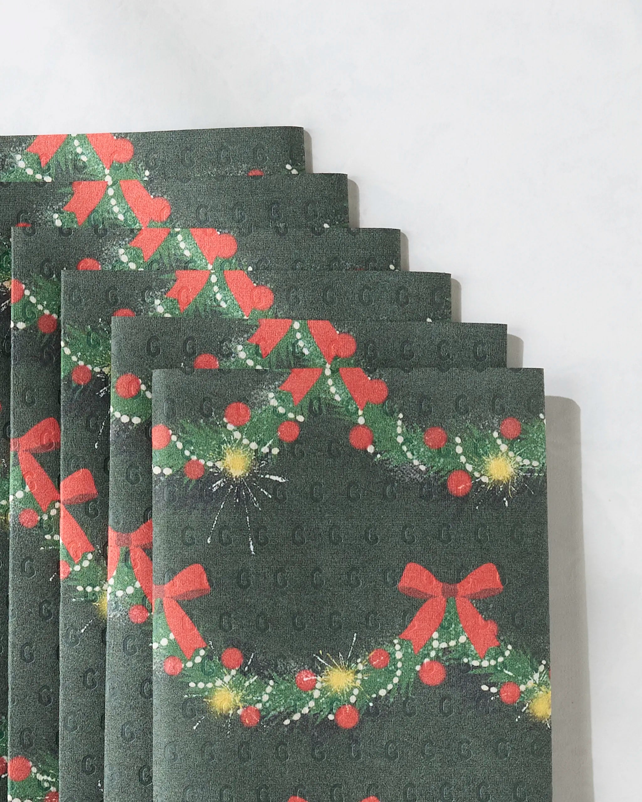 Five Geometry Yuletide Garland Not Paper Towels, reusable and dark green, are arranged in a fan. Each features festive red bows, holly leaves, berries, and yellow sparkles on a white background.