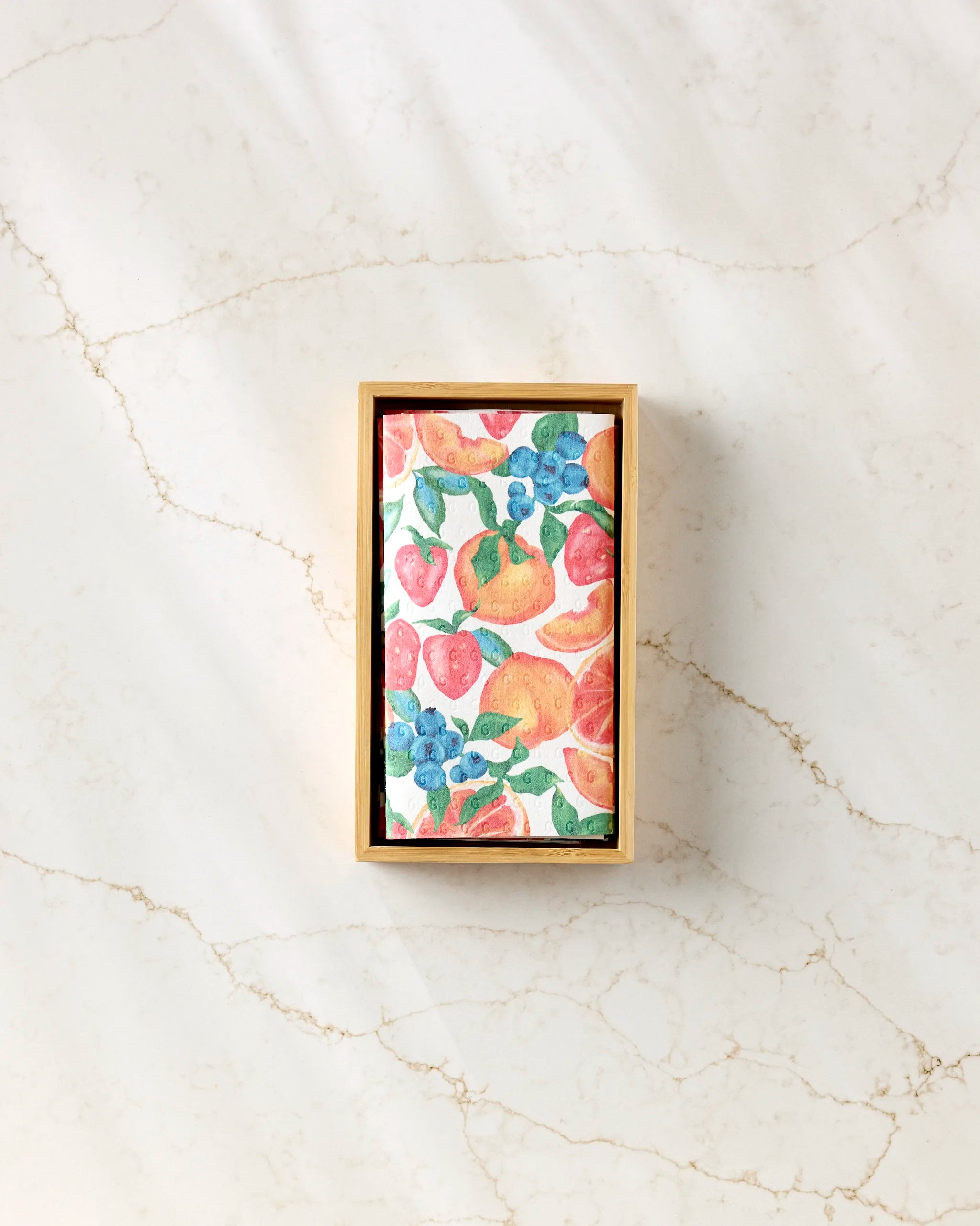 Aubrey Fairchild’s Zesty Life is a rectangular wooden box on marble, holding eco-friendly cards with colorful illustrations of strawberries, oranges, blueberries, and pears.