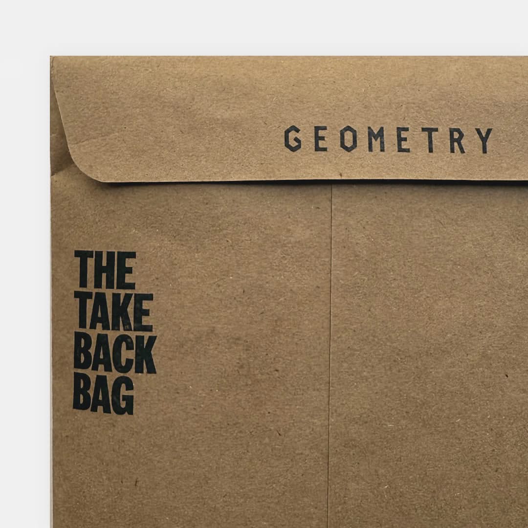 A brown paper envelope from GEOMETRY, called the Geometry Take Back Bag, features bold black text reading THE TAKE BACK BAG on the left and GEOMETRY near the top flap.