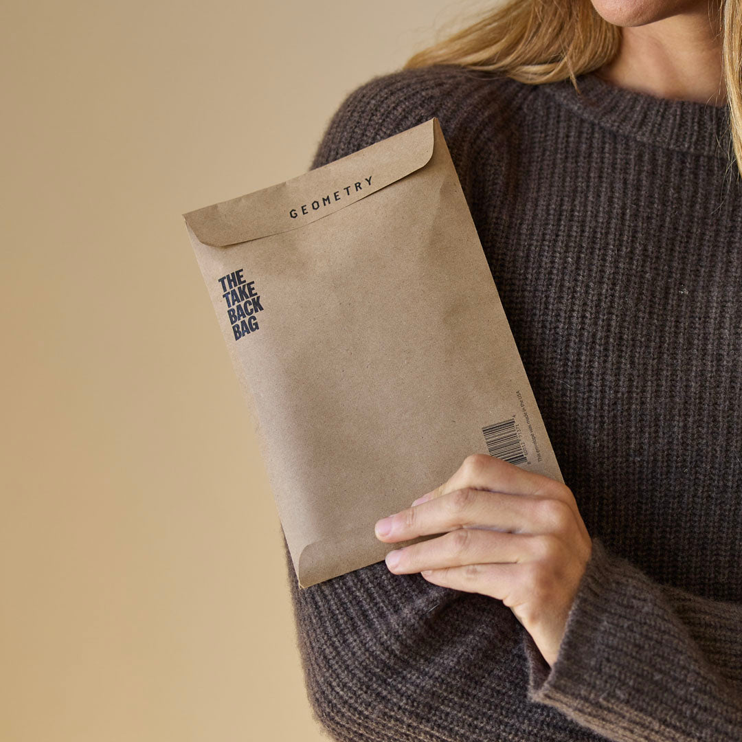 A person wearing a brown sweater holds the Geometry Take Back Bag by GEOMETRY against a neutral background.