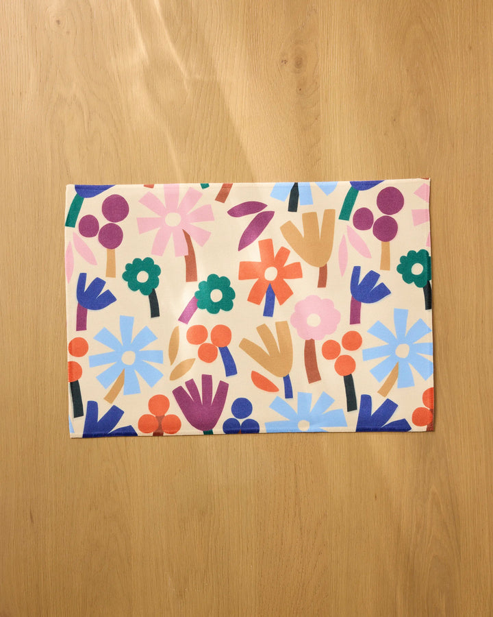 The Cool Flowers placemat by Jennifer Bouron features a vibrant, abstract floral design in blue, orange, pink, green, and purple on beige—machine washable and part of our Geometry Placemats collection.
