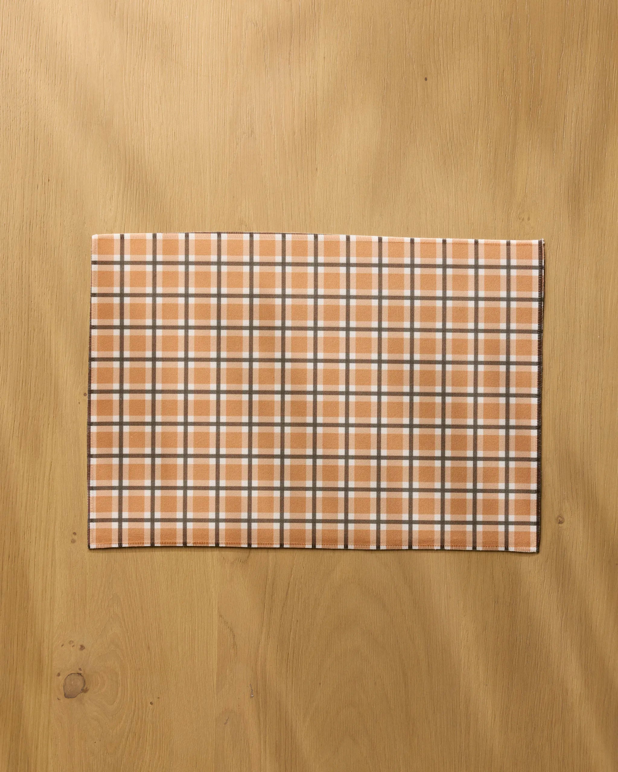 The Geometry Country Pantry rectangular recycled placemat, featuring a beige, white, and gray plaid pattern, is displayed on a light wood surface.