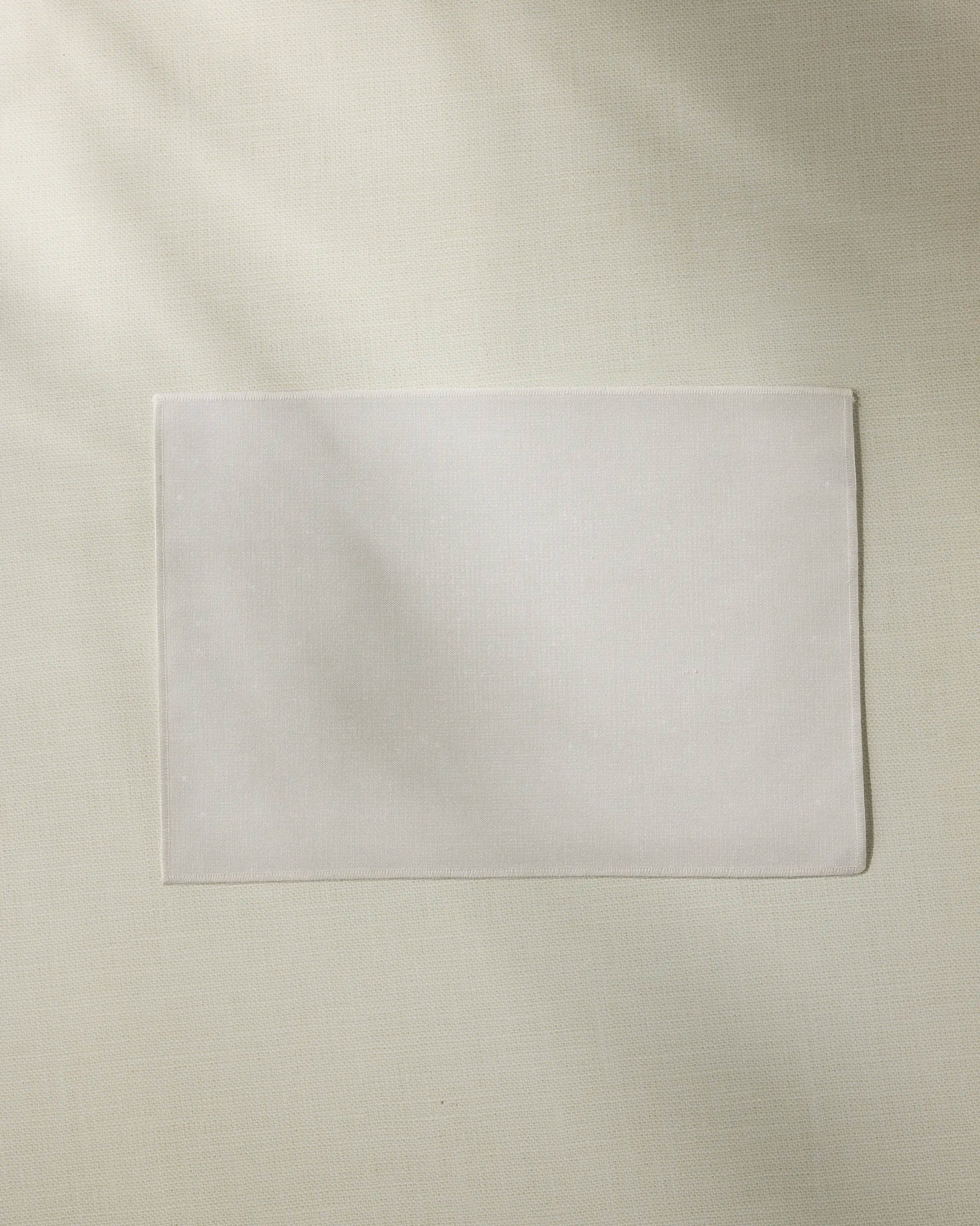 The Geometry Frost rectangular white cloth napkin is neatly placed on a light beige textured surface next to eco-friendly placemats, perfect for sustainable dining.