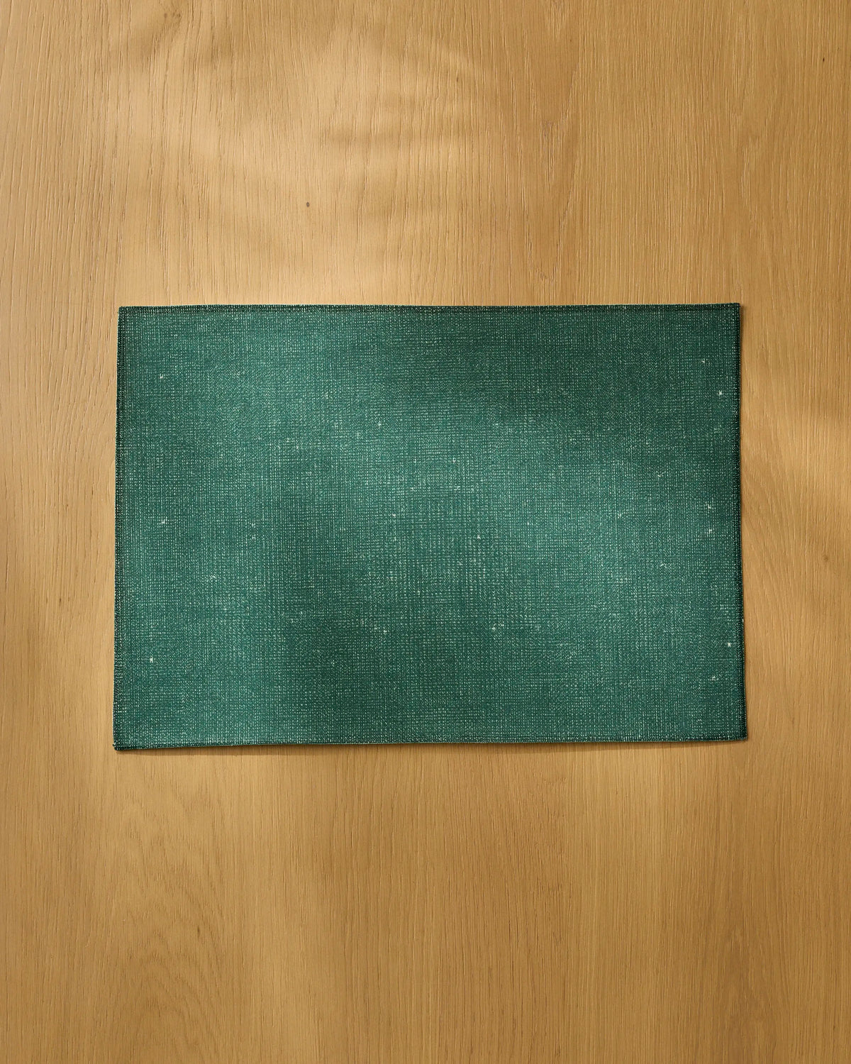 A rectangular Gather placemat by Geometry in green, made from eco-friendly materials, is centered on a wooden table with a light brown finish.