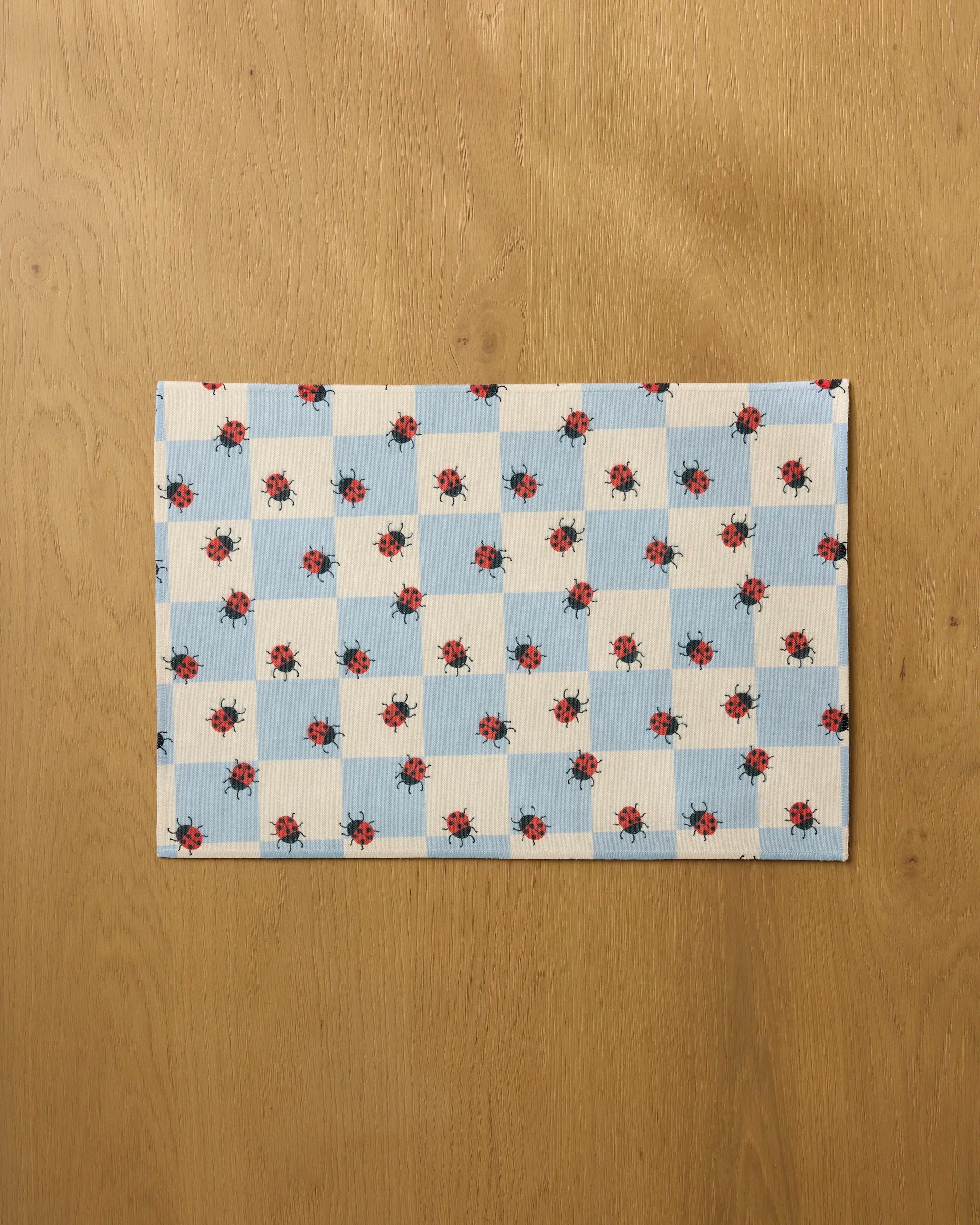 The Mariquita Pop placemat by Geometry features a blue and white checkerboard with red floral accents. Placed on light wood, it’s both stylish and practical—plus, it’s machine washable for easy cleaning.