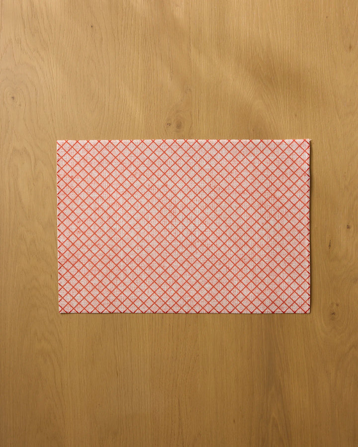 The Market Check cleaning cloth by Geometry, featuring a red diamond pattern, lies flat on a light wooden surface—combining practical use with decorative style.