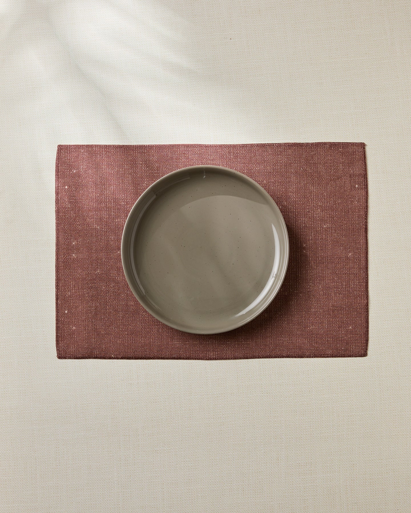 The Geometry Russet eco-friendly placemat in maroon, with a beige ceramic plate on top, rests on a light tablecloth, captured from above for a simple, minimalistic look.