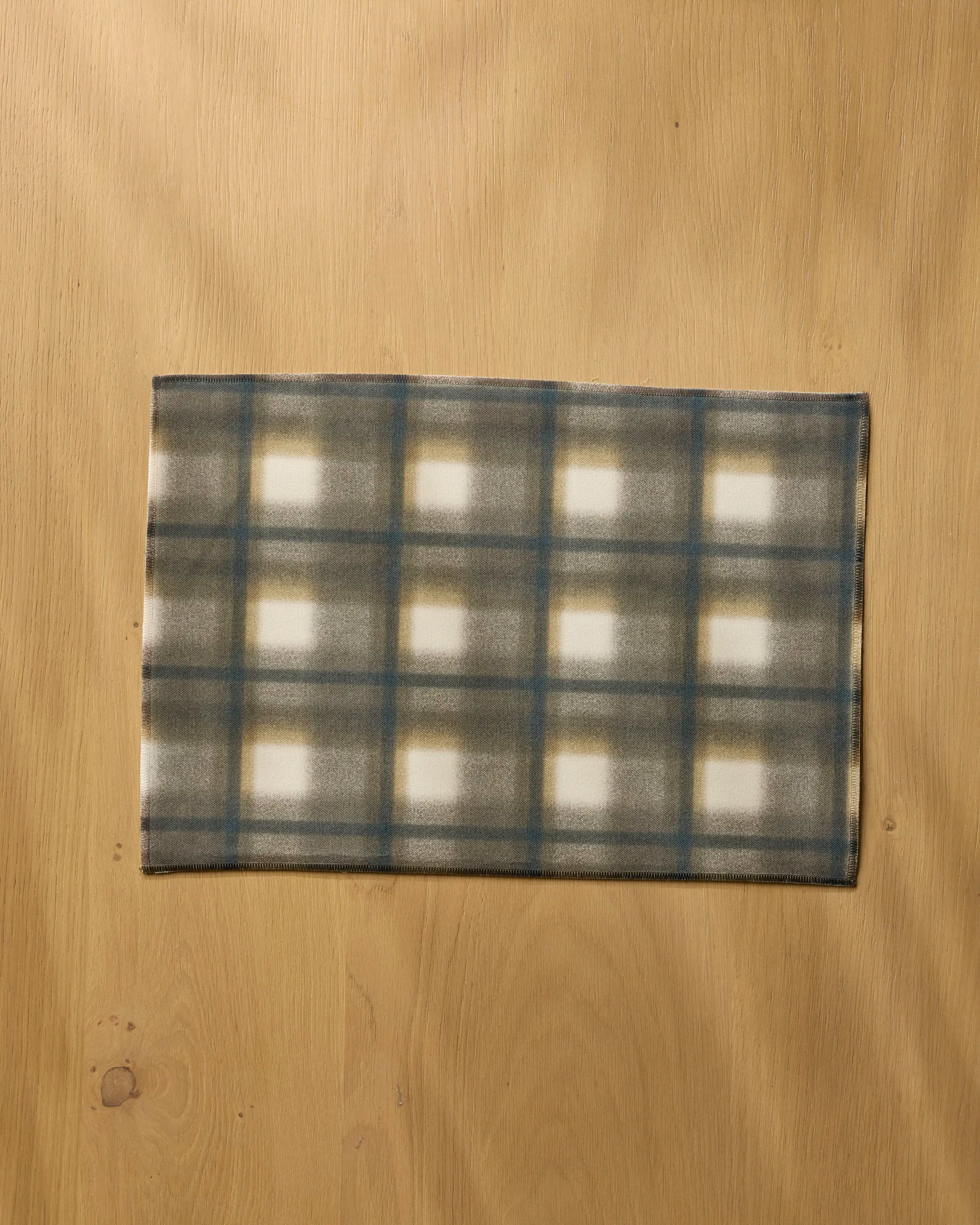 The Geometry Toasted placemat features a rectangular plaid design in muted green, blue, and beige—eco-friendly and perfect for adding sustainable style to your dining table.