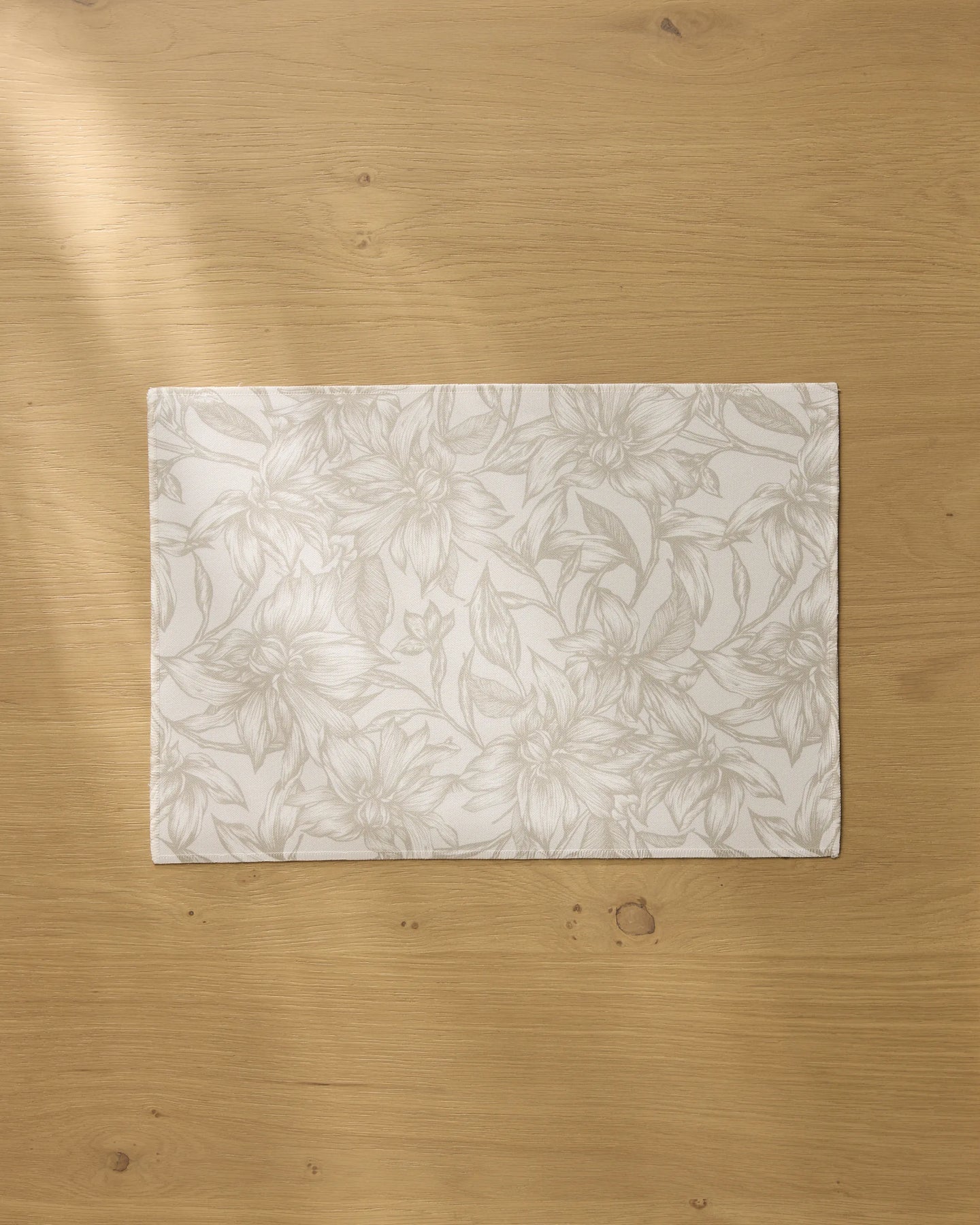 The Geometry Alba rectangular white recycled placemat, featuring a subtle floral pattern, rests on a light wooden table bathed in soft natural light.